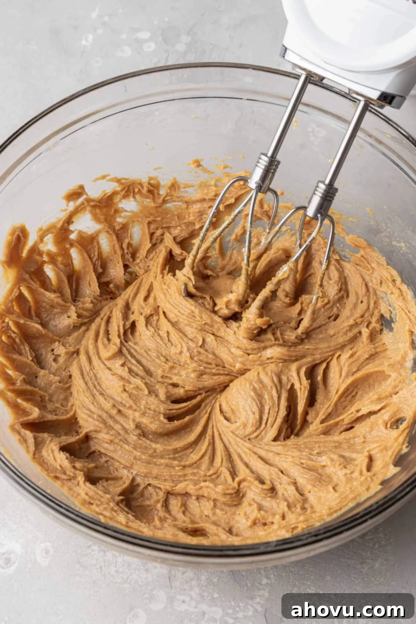 The wet ingredients for peanut butter cookie dough in a glass mixing bowl, with an electric beater. 
