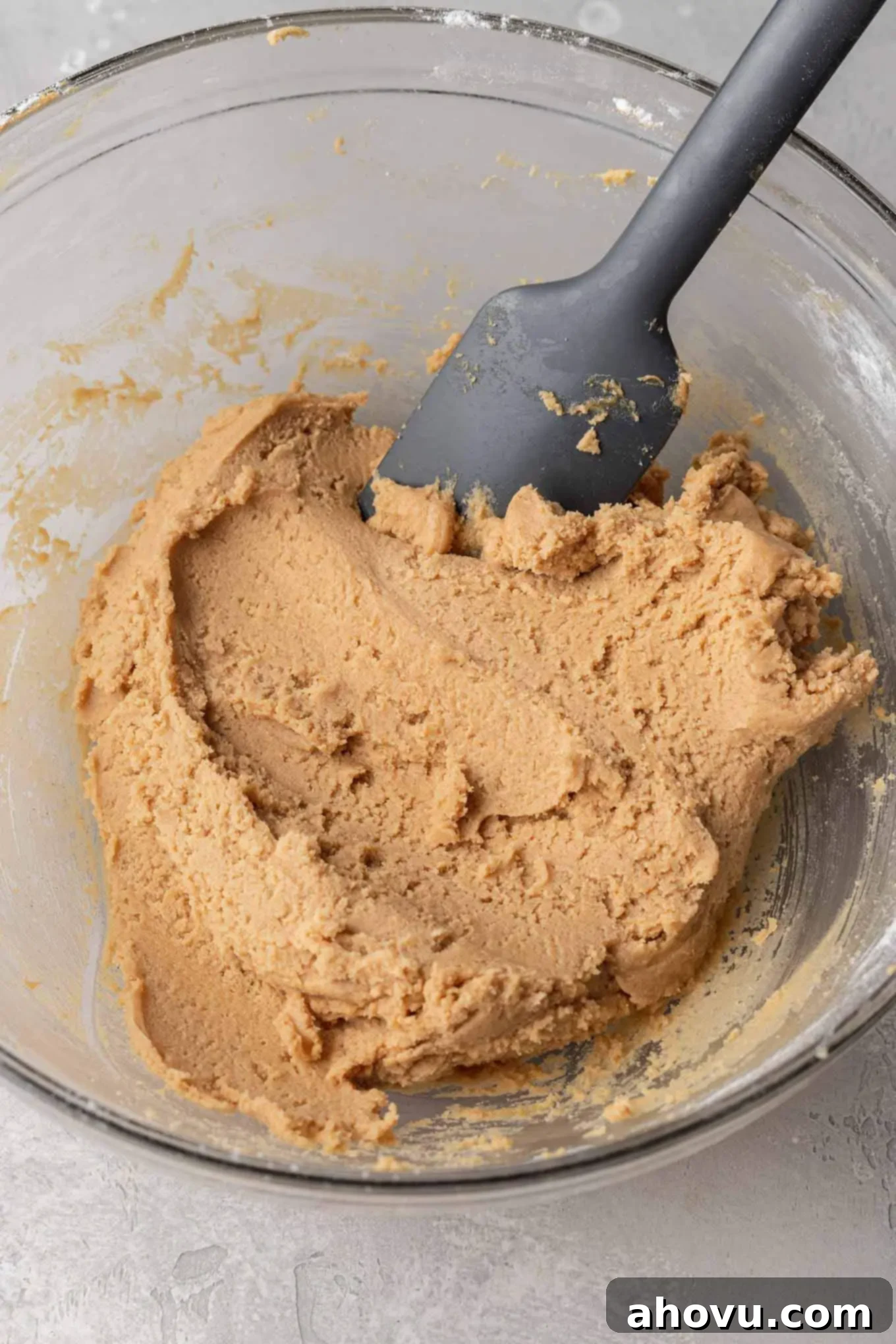 Peanut butter cookie dough in a glass mixing bowl, with a rubber spatula. 