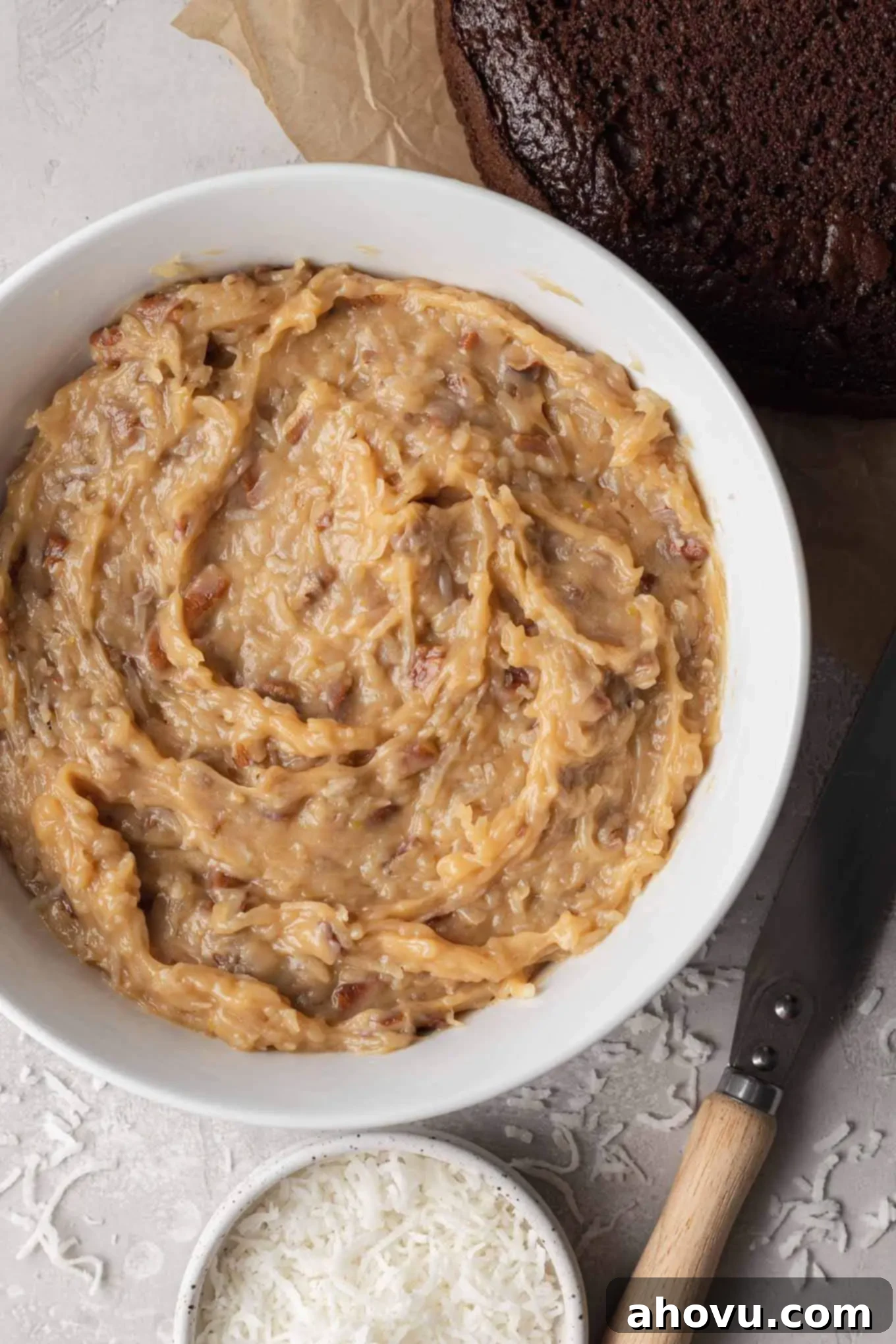 An overhead view of German chocolate cake frosting in a bowl, showcasing its rich texture with pecans and coconut.
