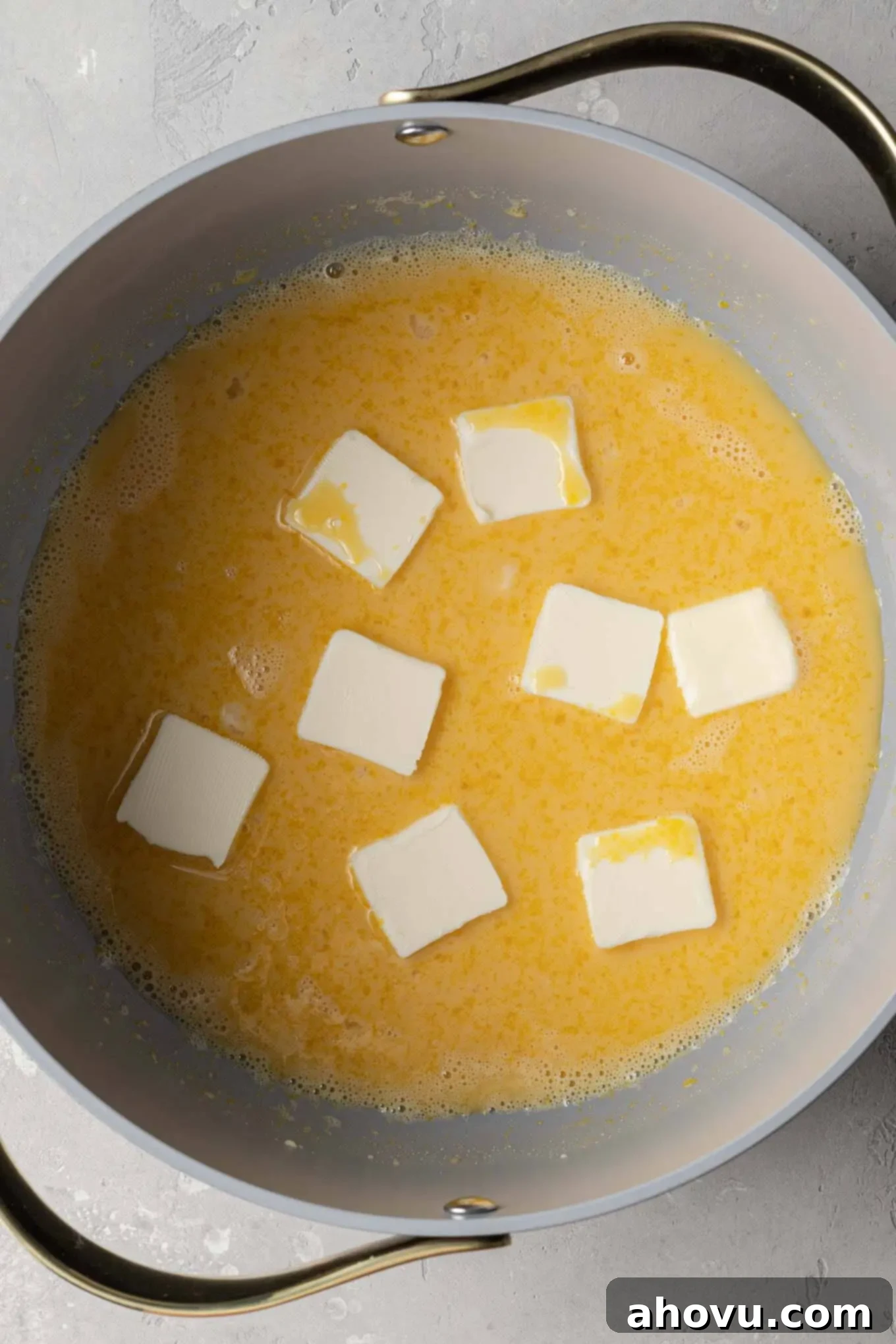 An overhead view of an egg yolk, butter, sugar, and evaporated milk mixture in a saucepan before cooking.