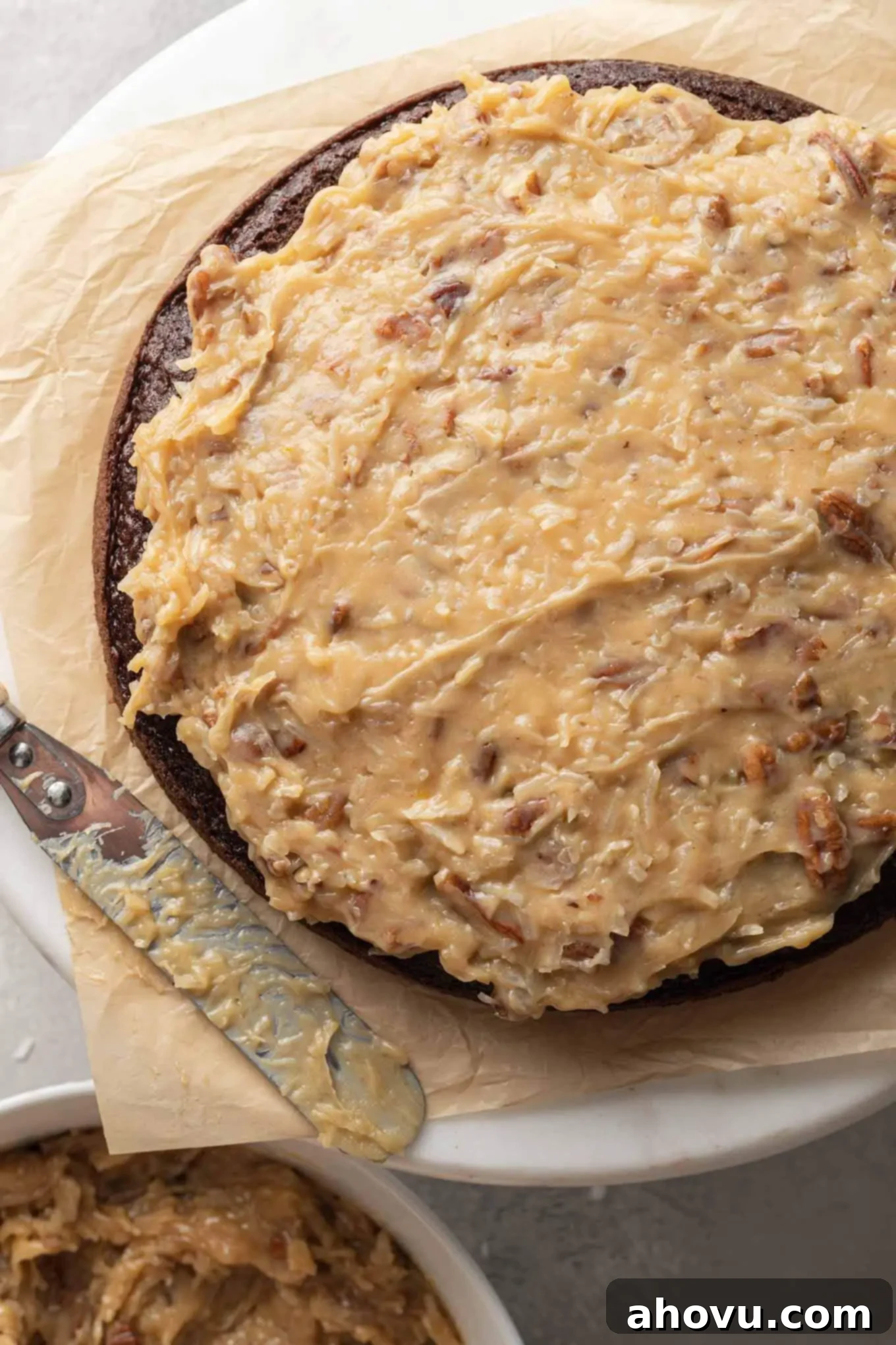 An overhead view of a German chocolate cake being frosted with a thick layer of homemade frosting.