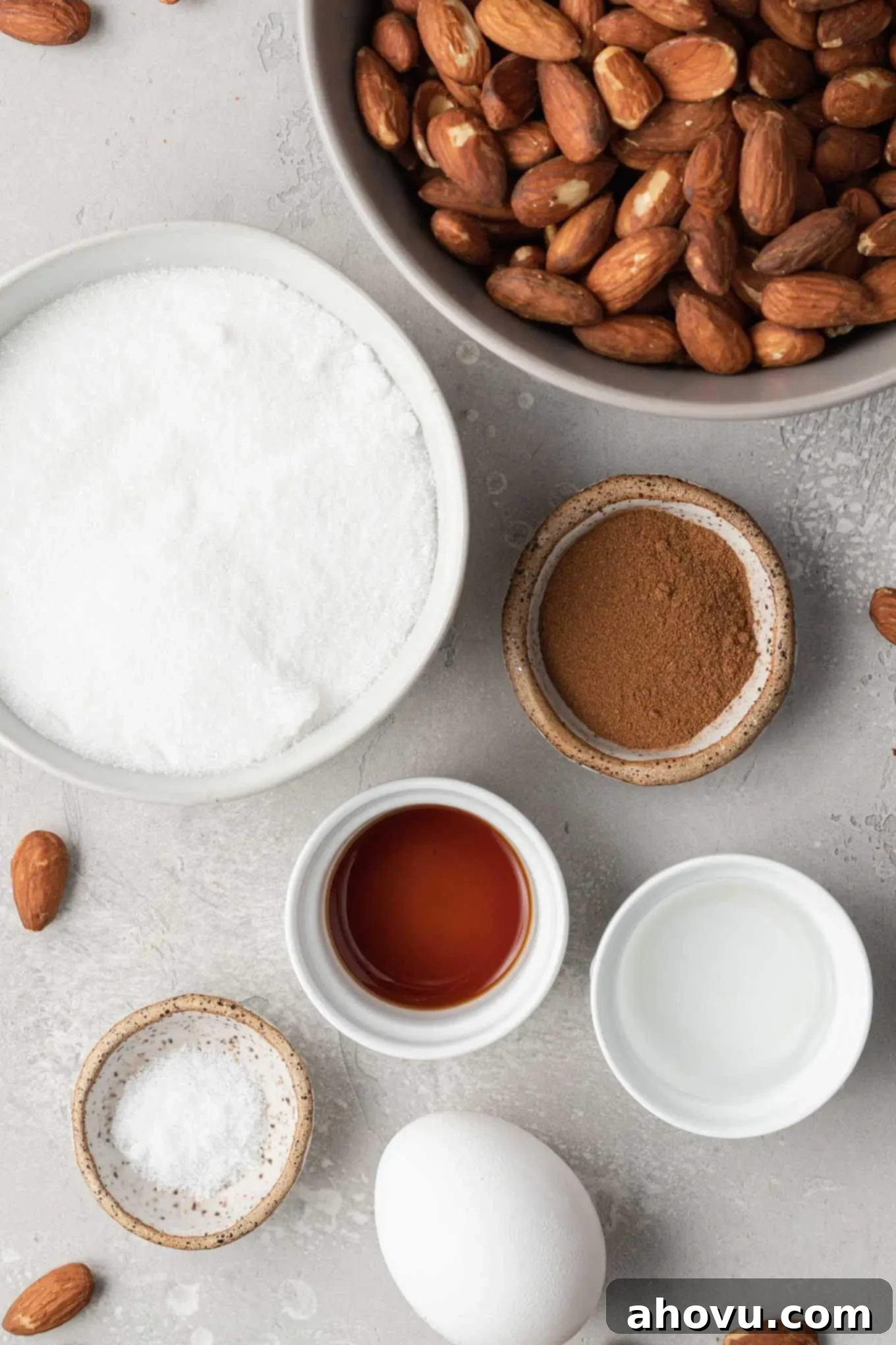 An overhead shot displaying the essential ingredients for making candied almonds: raw almonds, sugar, cinnamon, salt, vanilla extract, and an egg white.