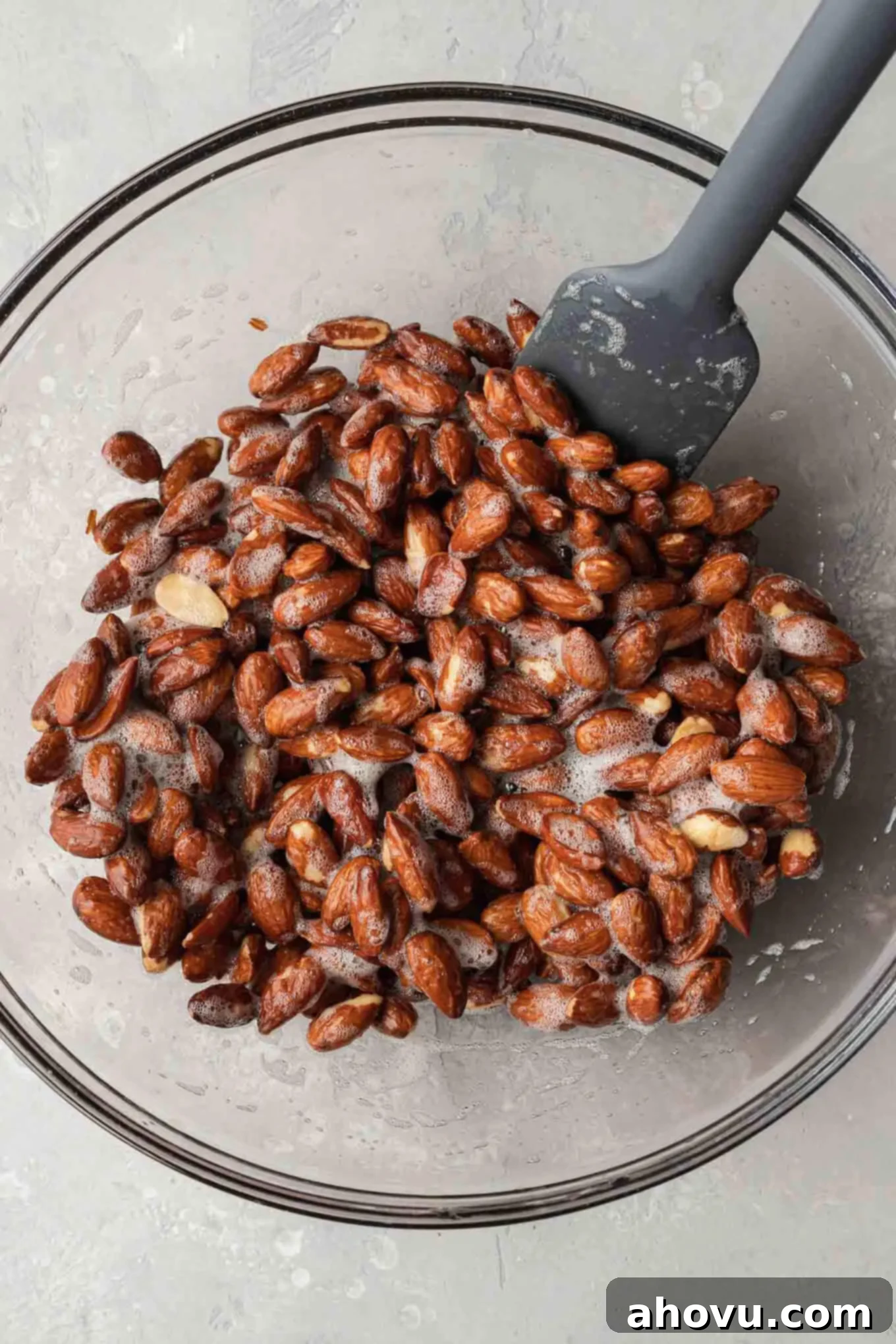 An overhead view of raw almonds being mixed with an egg white mixture in a large bowl, ensuring even coating.