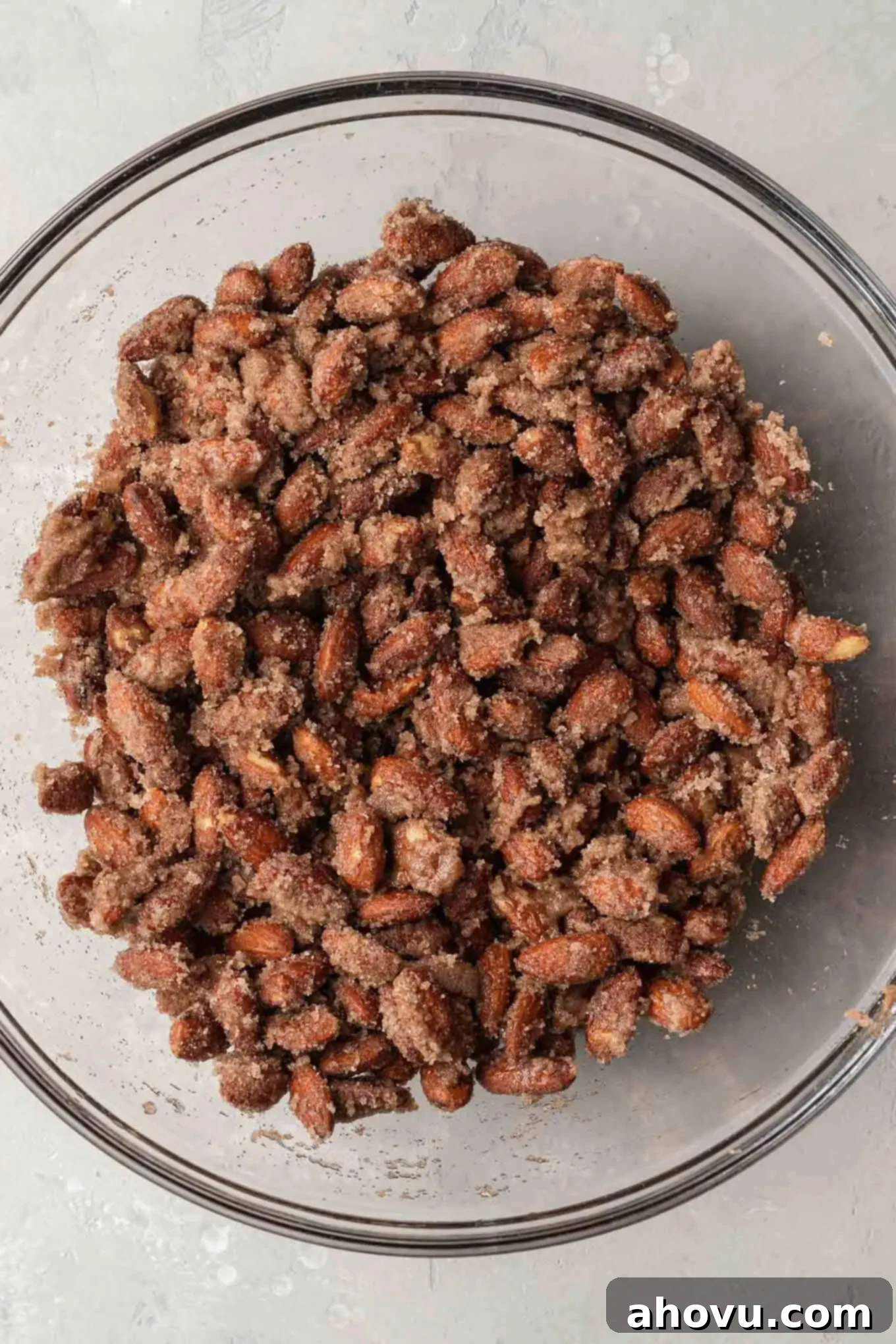 An overhead view of almonds fully coated in a cinnamon sugar mixture in a mixing bowl, prior to being spread on a baking sheet.