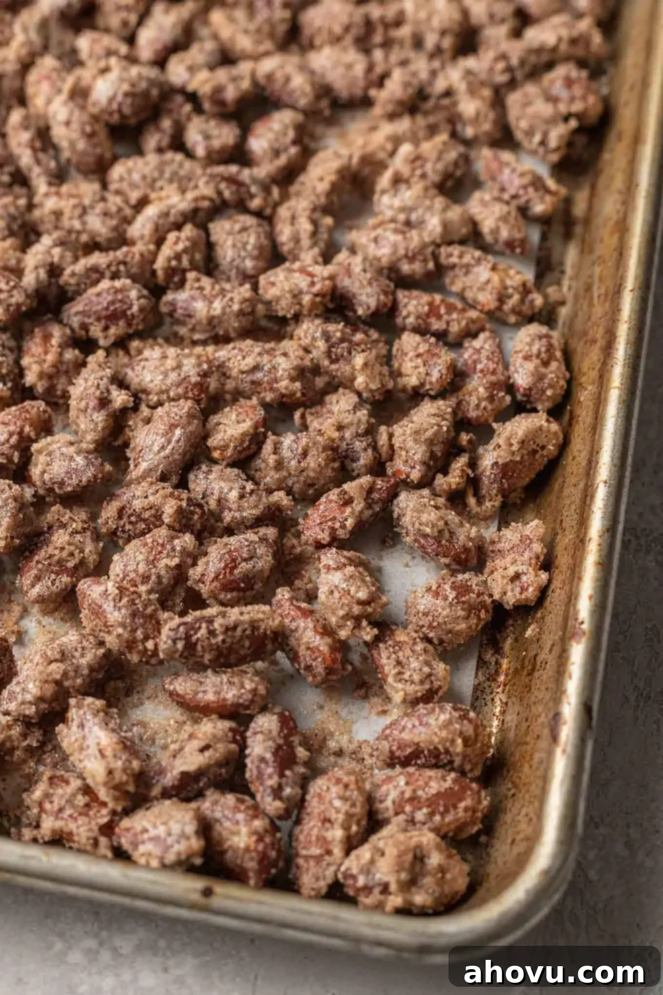 Freshly baked cinnamon candied almonds on a parchment paper-lined baking sheet, glistening with their crispy coating.