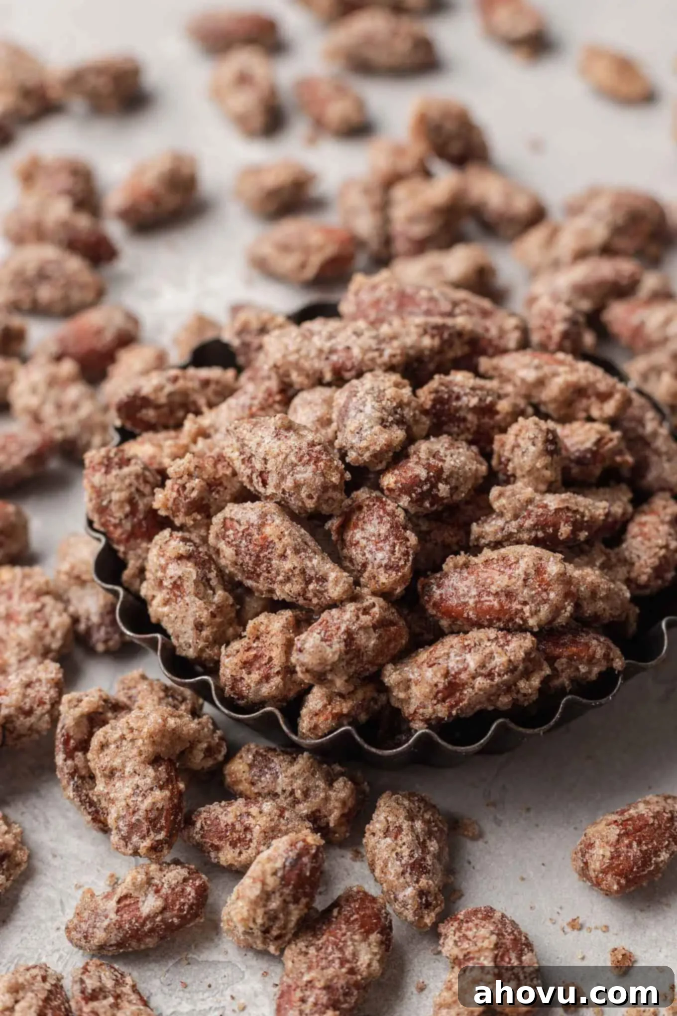 A small rustic dish filled with glistening sugared almonds, with more scattered around on a wooden surface, ready for snacking.
