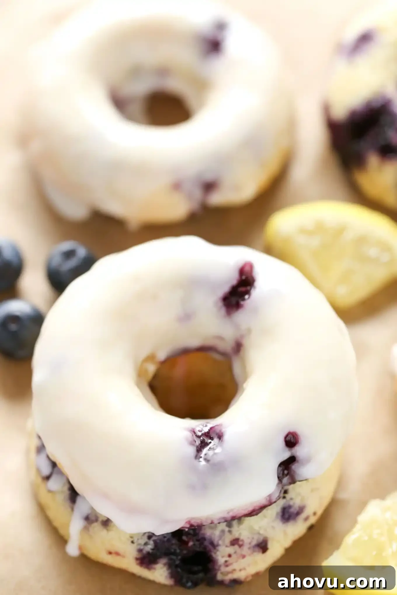 Zesty Lemon Blueberry Baked Donuts 3 A closeup view of a lemon blueberry cake donut topped with glaze. Another donut and some berries rest in the background.