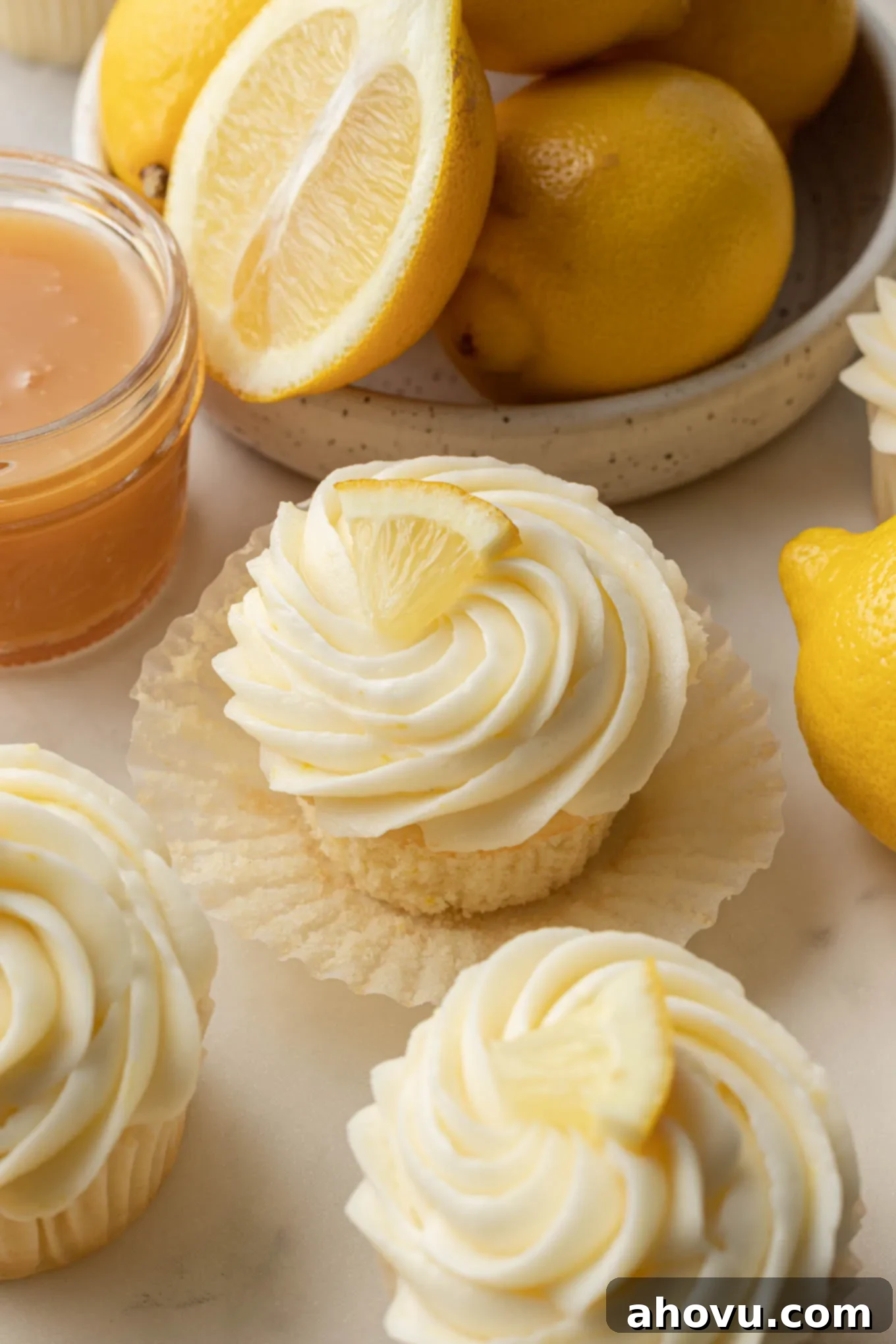 Freshly baked lemon cupcakes in decorative liners, artfully arranged and surrounded by vibrant whole and sliced lemons, highlighting their zesty essence. 