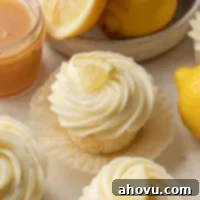 Perfectly piped lemon cupcakes, adorned with a fresh lemon wedge, beside a rustic bowl of lemons and a jar of homemade lemon curd, all ready for a delightful spring or summer treat.
