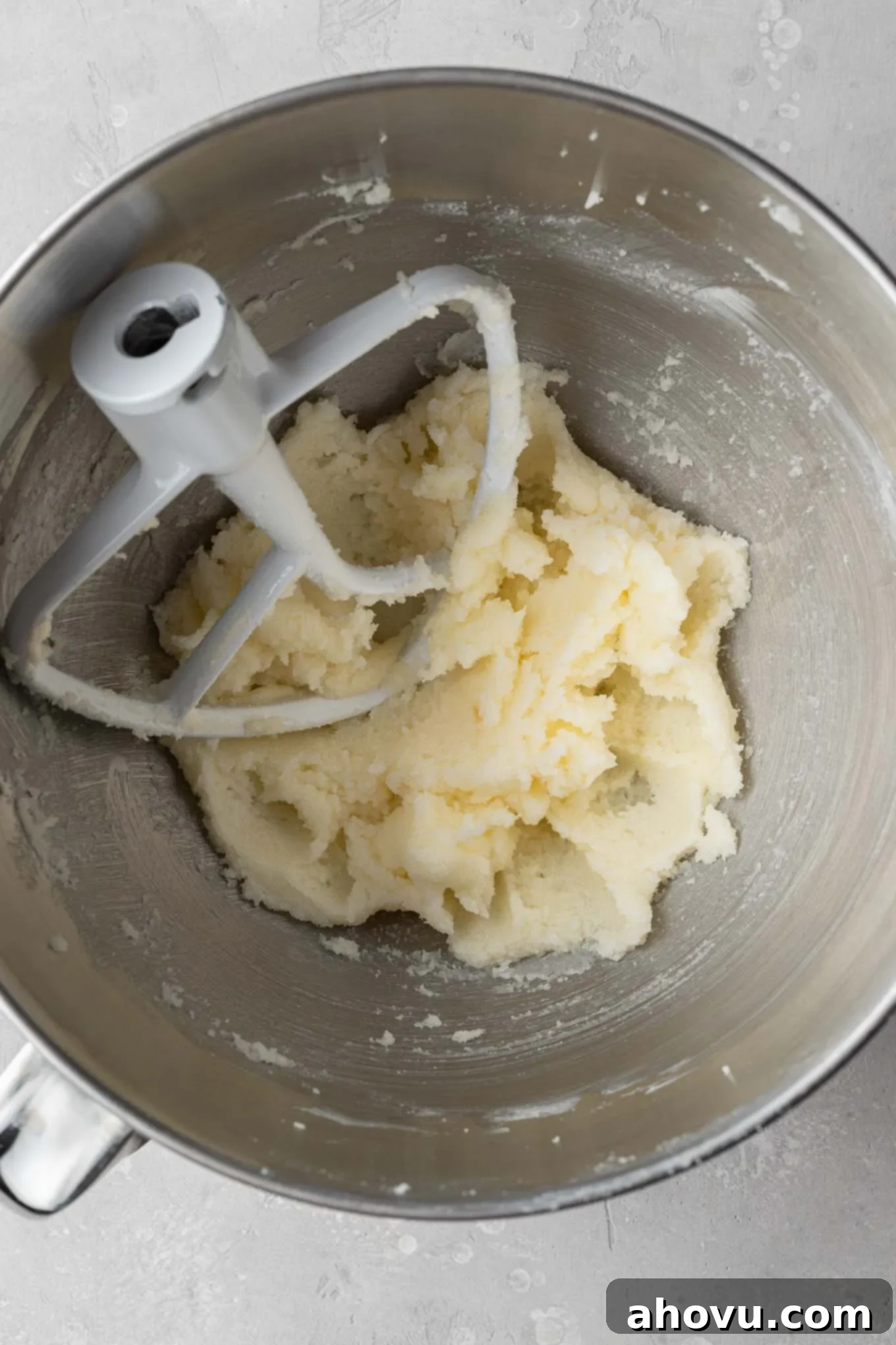 An overhead view of creamy, light yellow butter and white granulated sugar being perfectly creamed together in a mixing bowl, indicative of the first step in baking.