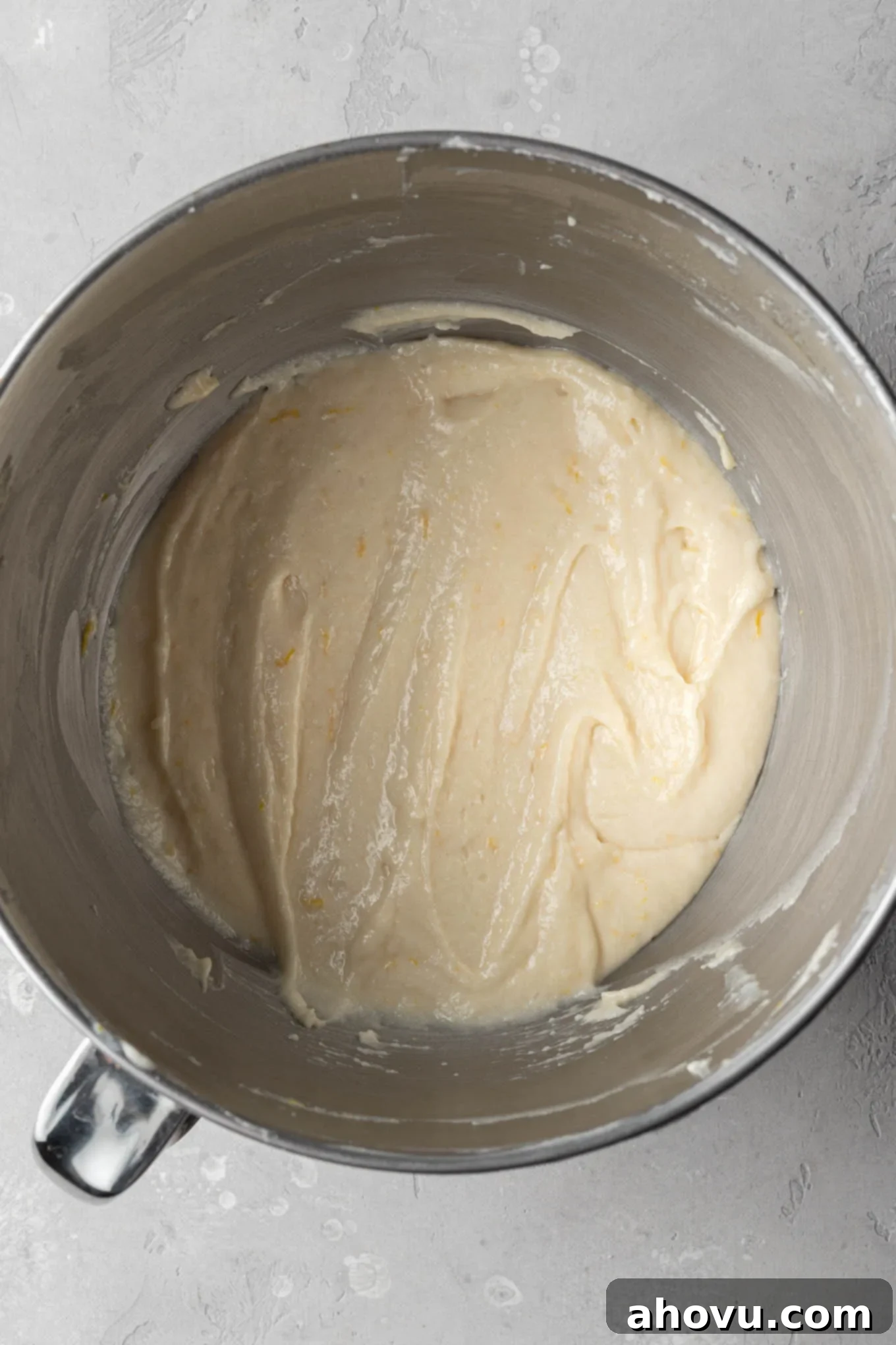 An overhead view of a mixing bowl containing smooth, pale yellow lemon cupcake batter, perfectly combined and ready for baking.