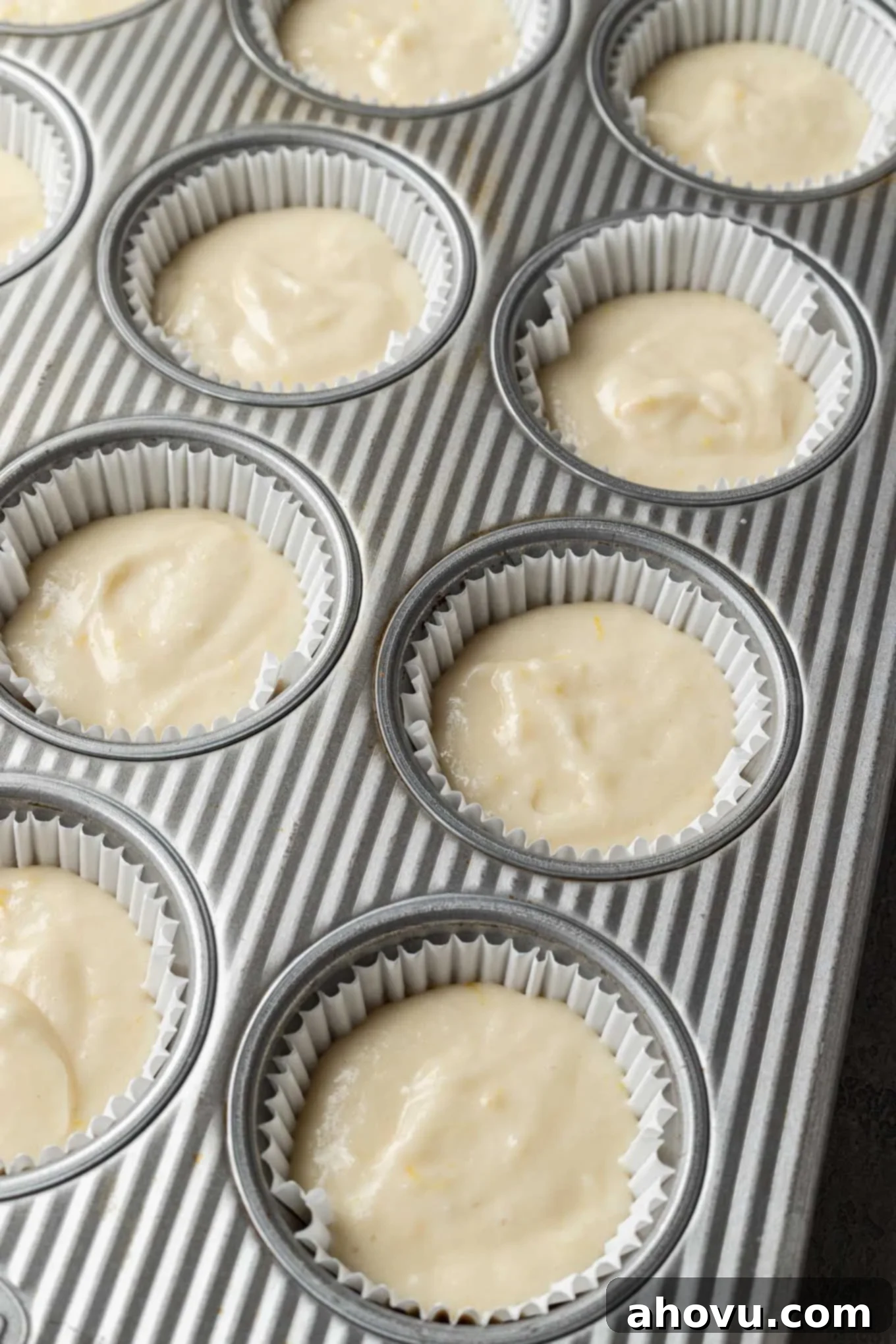 Lemon cupcake batter meticulously spooned into individual lined muffin tins, awaiting their transformation in the oven.