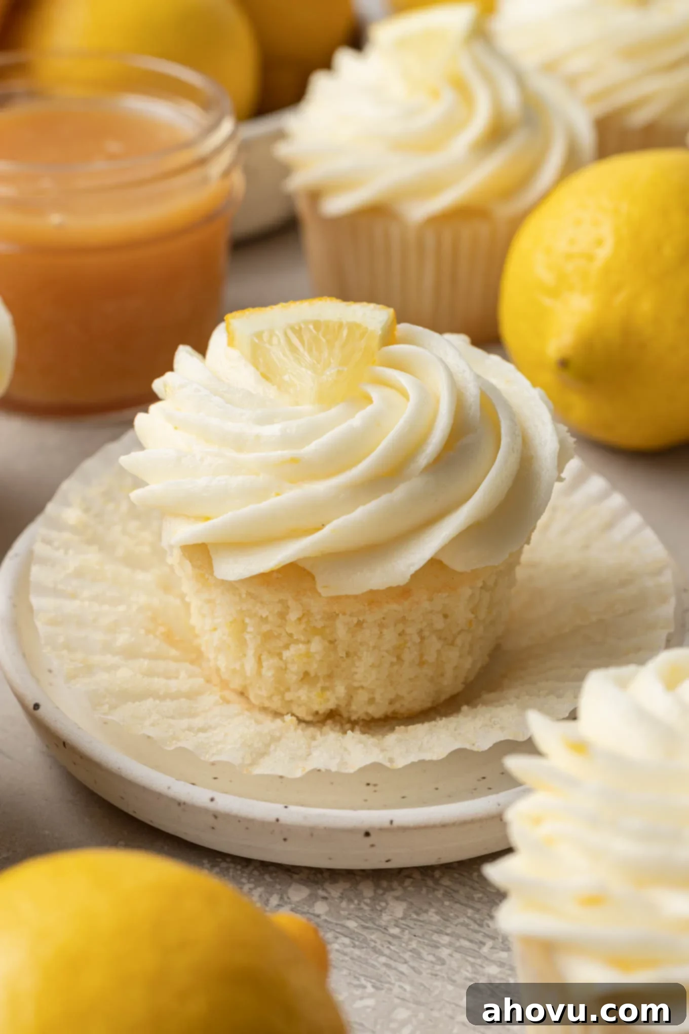 A detailed close-up of a lemon-filled cupcake, with its paper liner elegantly pulled down to reveal the soft, moist crumb and the generous, vibrant lemon curd filling at its core.
