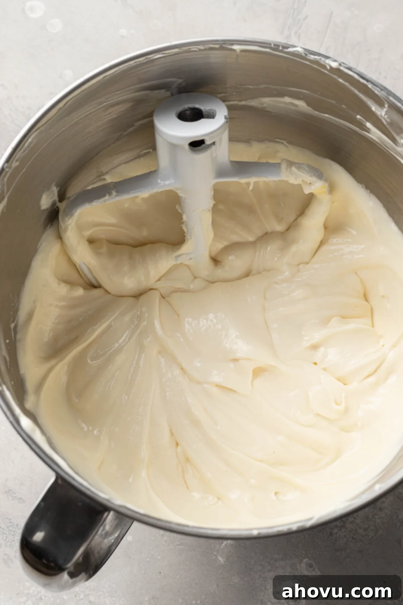 An overhead view of raw cheesecake filling in a mixing bowl, with a paddle attachment.
