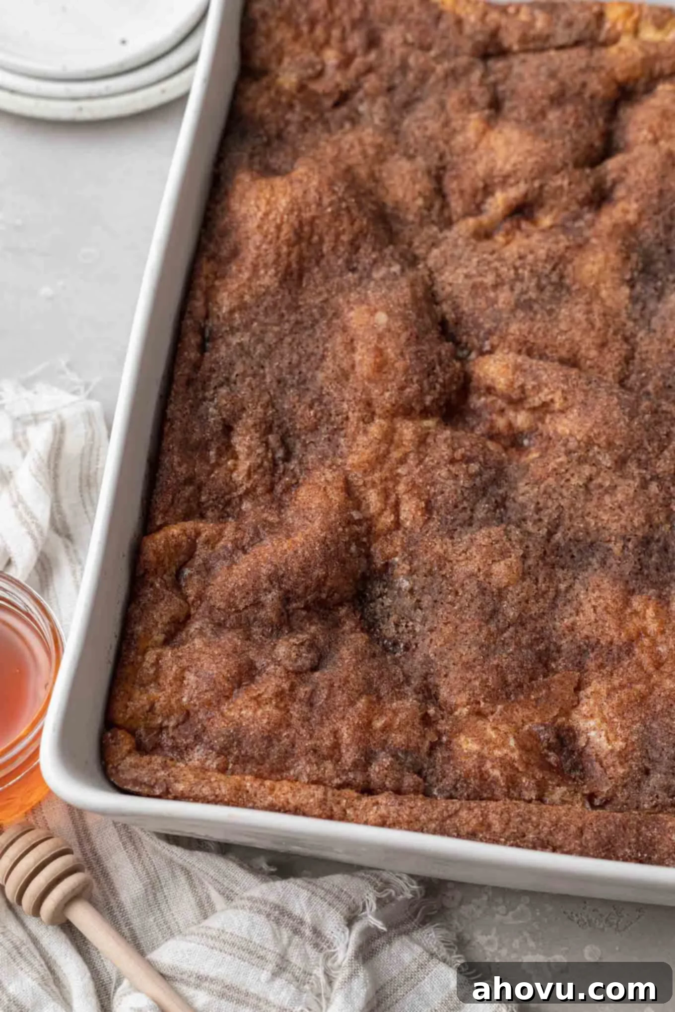 Baked sopapilla cheesecake in a large casserole dish. A jar of honey rests on the side.