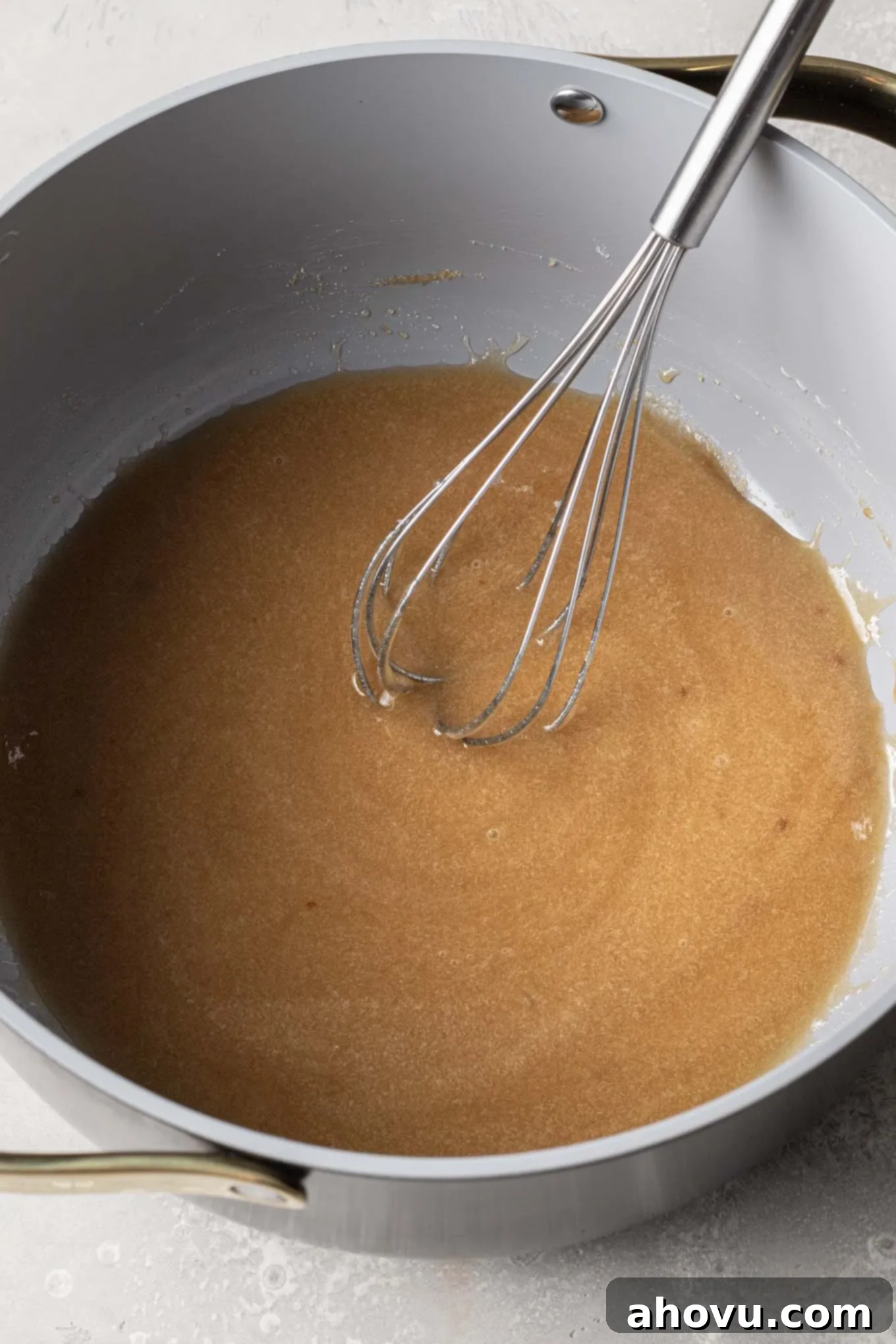 An overhead view of corn syrup and sugar being heated in a saucepan, with a whisk ready for stirring.