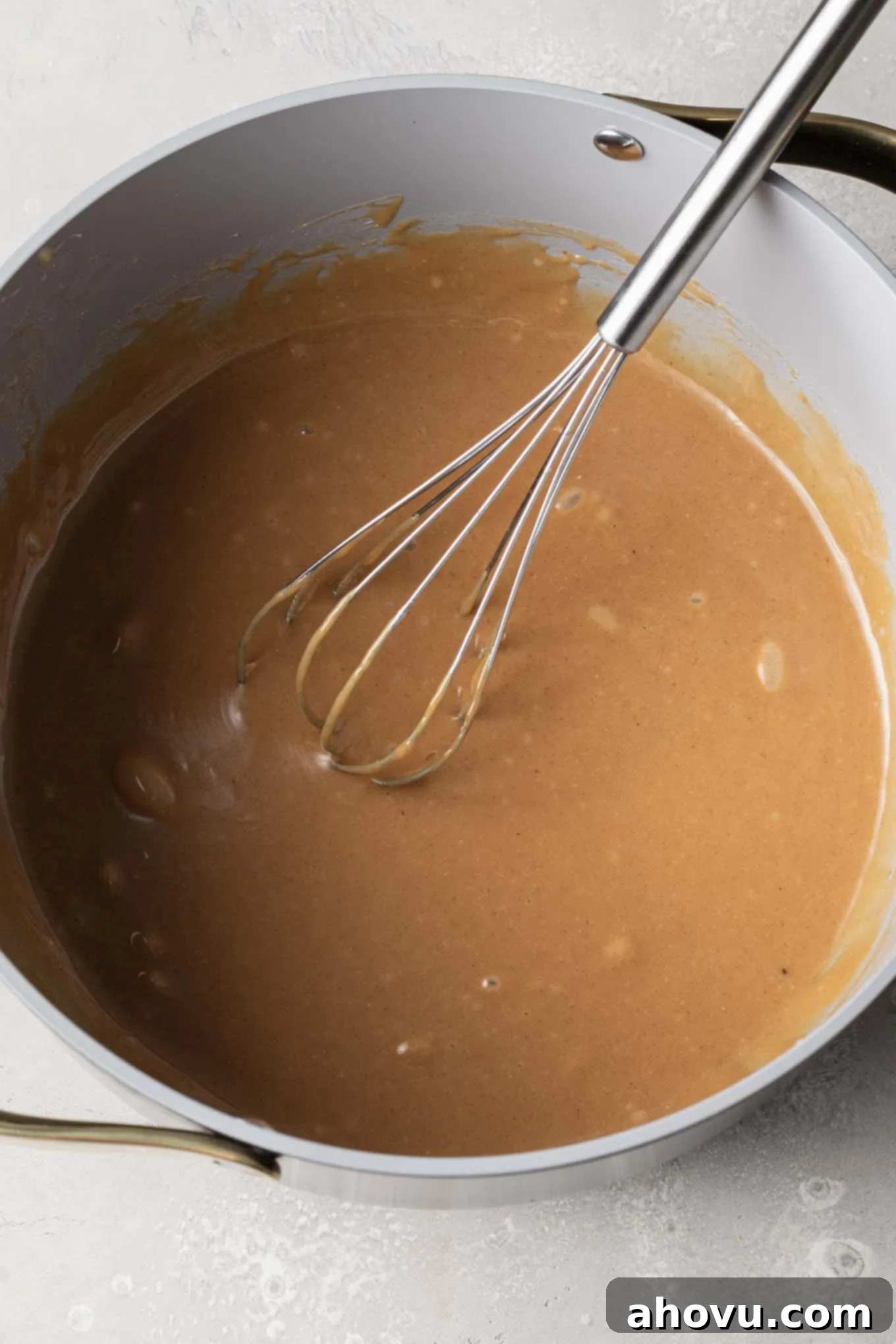 An overhead view of the creamy peanut butter mixture seamlessly incorporated into the warm sugar mixture in a saucepan, with a whisk.