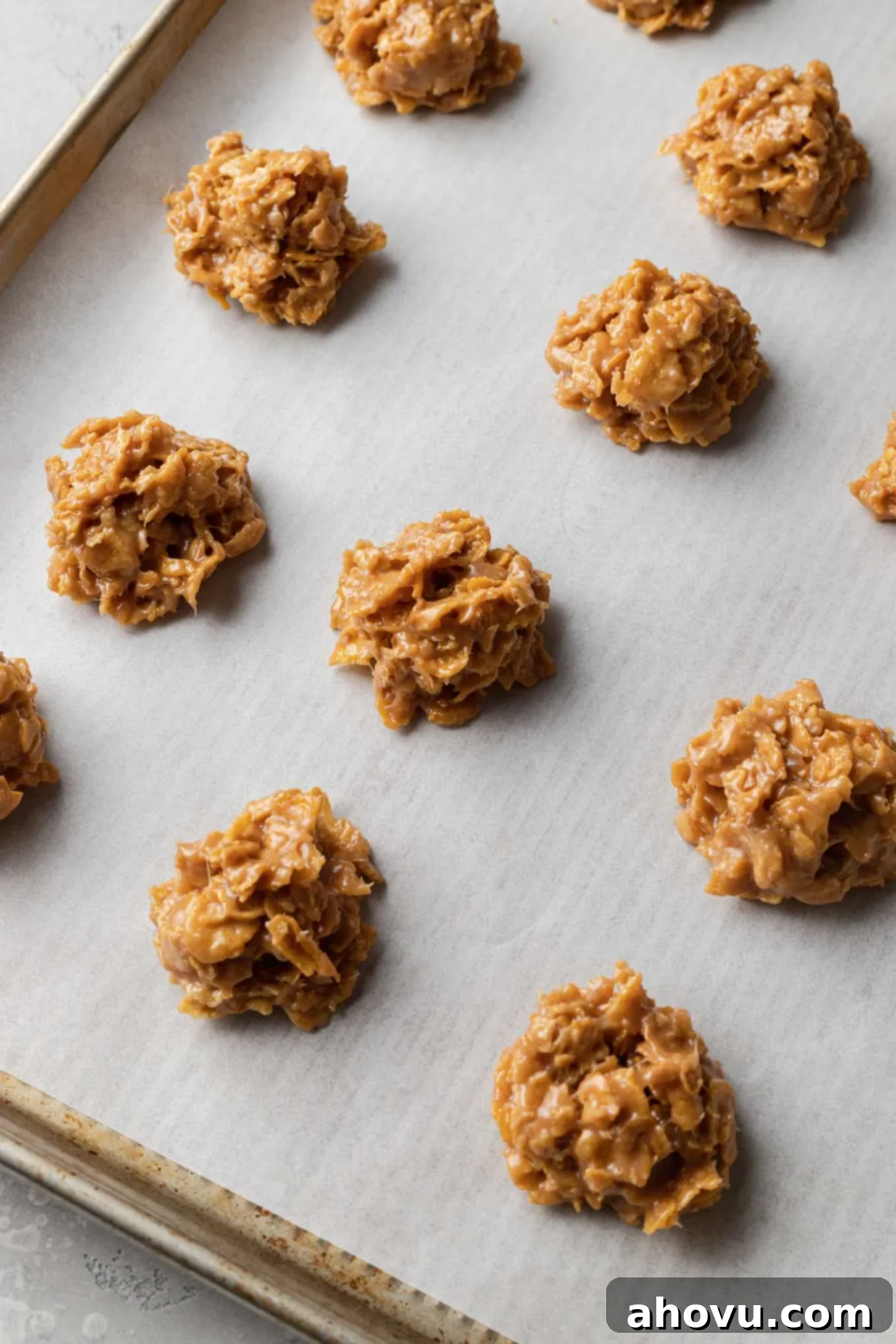 A parchment paper-lined baking sheet showcasing three perfectly formed rows of delectable cornflake cookie balls, waiting to set.