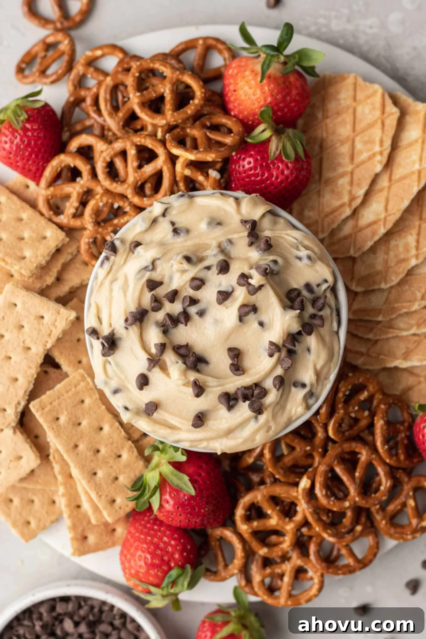 Dreamy Cookie Dough Dip 2 An overhead view of a dish of chocolate chip cookie dough dip on a platter with pretzels, graham crackers, and berries.