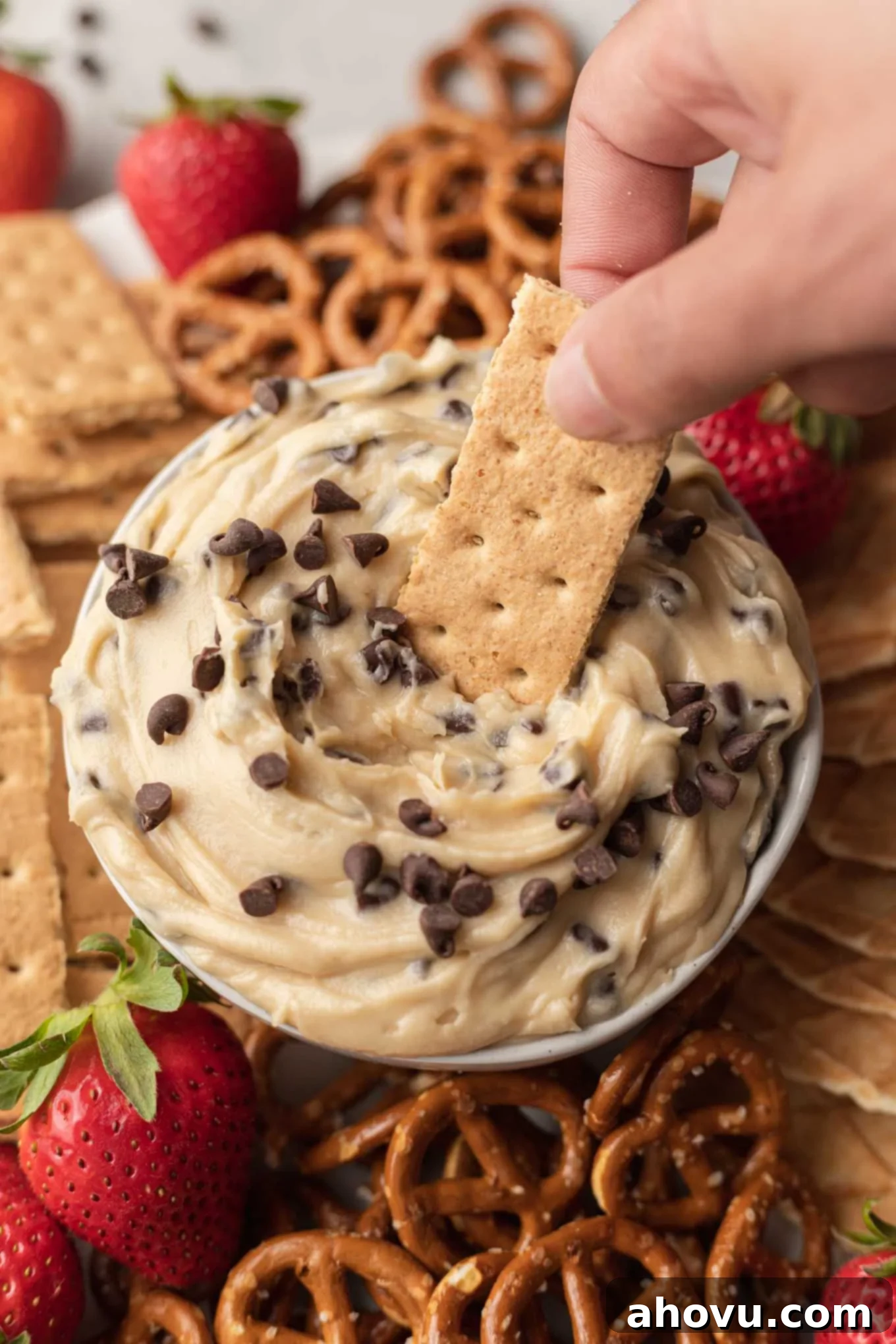 Dreamy Cookie Dough Dip 10 A graham cracker being dipped into chocolate chip cookie dough dip, which rests on a platter.