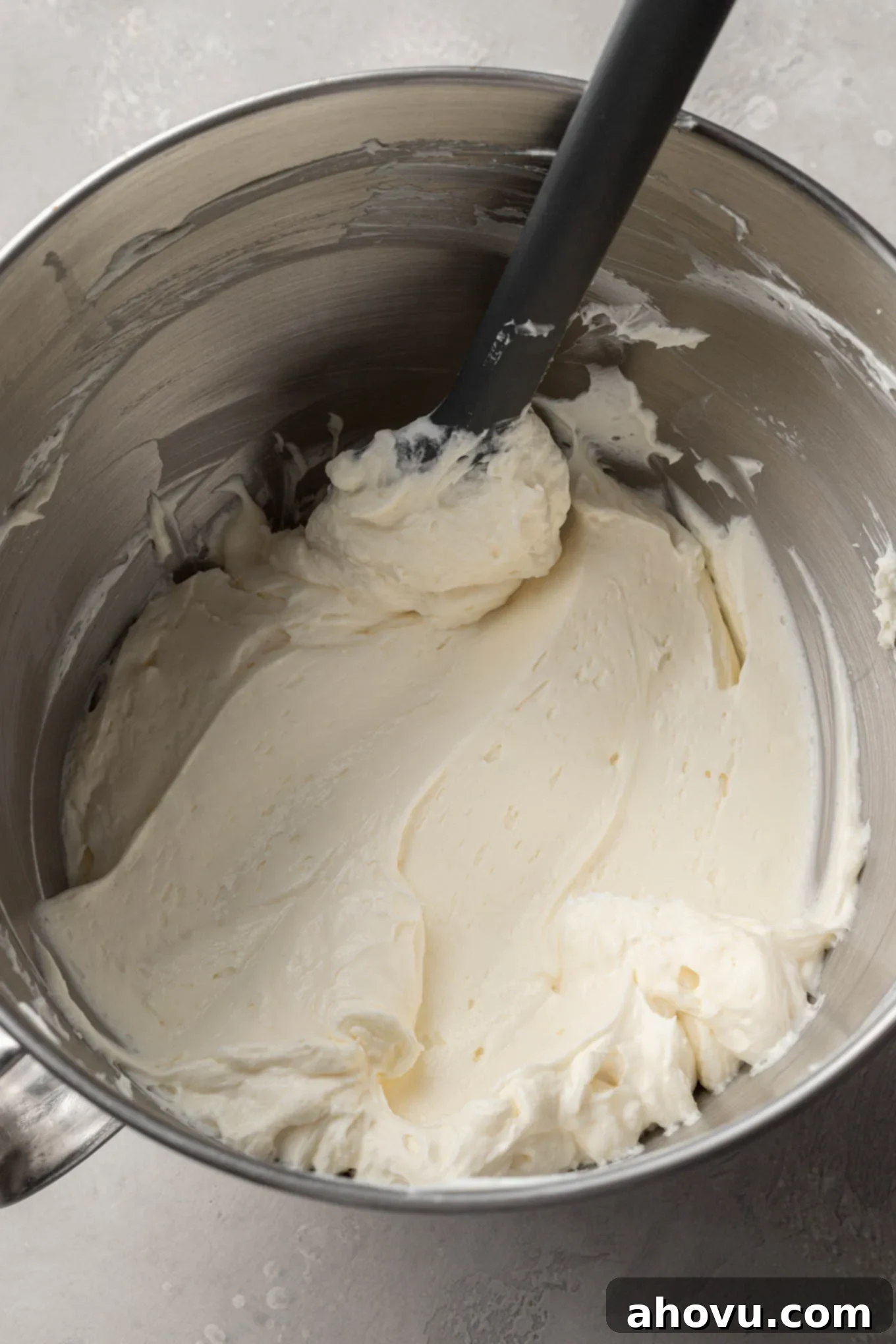 An overhead view of the cheesecake mixture in a mixing bowl, with a rubber spatula. 