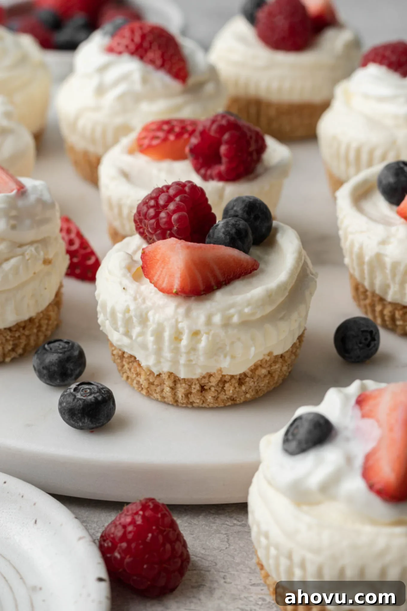 Mini no-bake cheesecakes topped with fresh berries on a white platter. 
