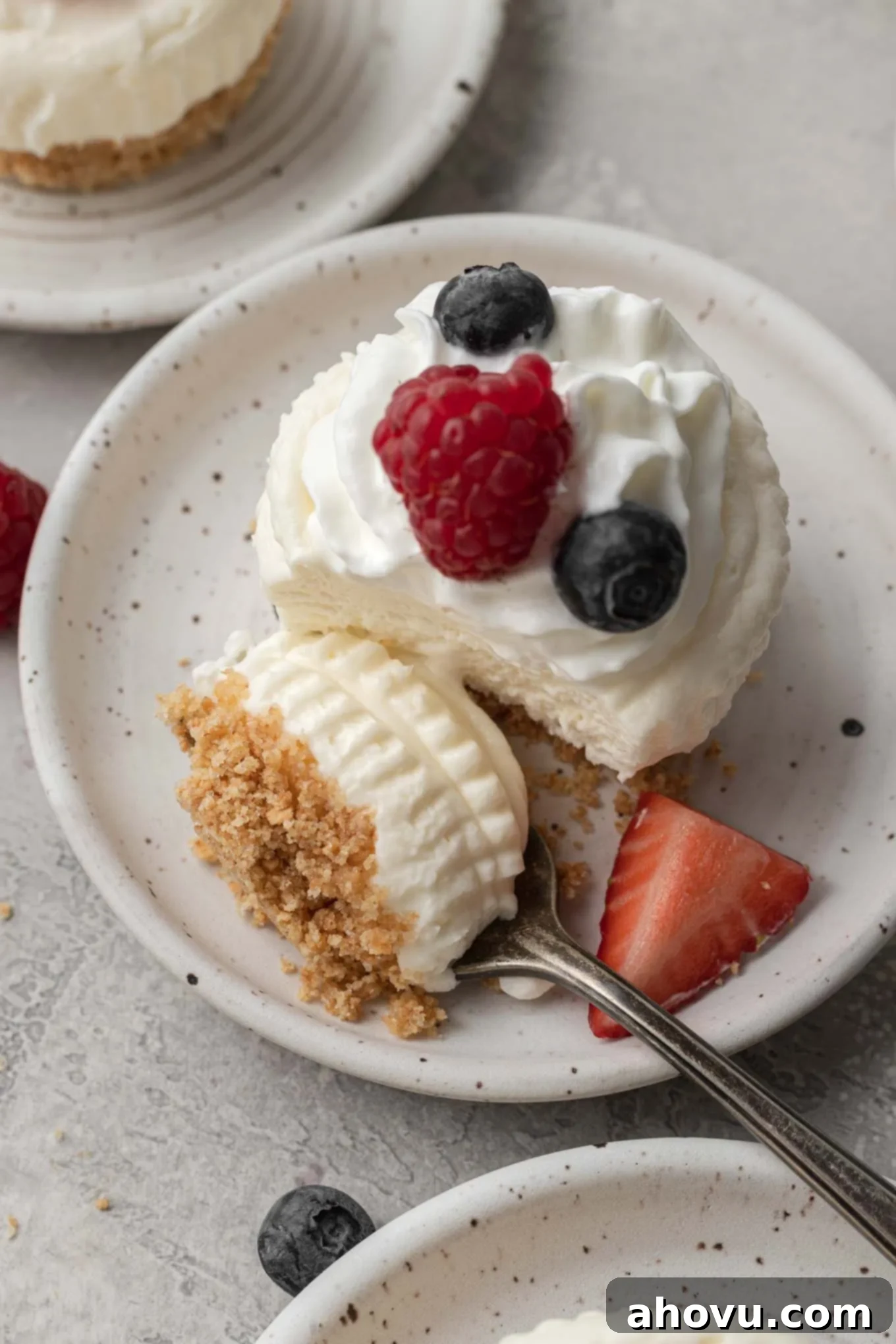 An overhead view of an individual no-bake cheesecake topped with whipped cream and fresh berries. A bite has been speared onto a fork. 