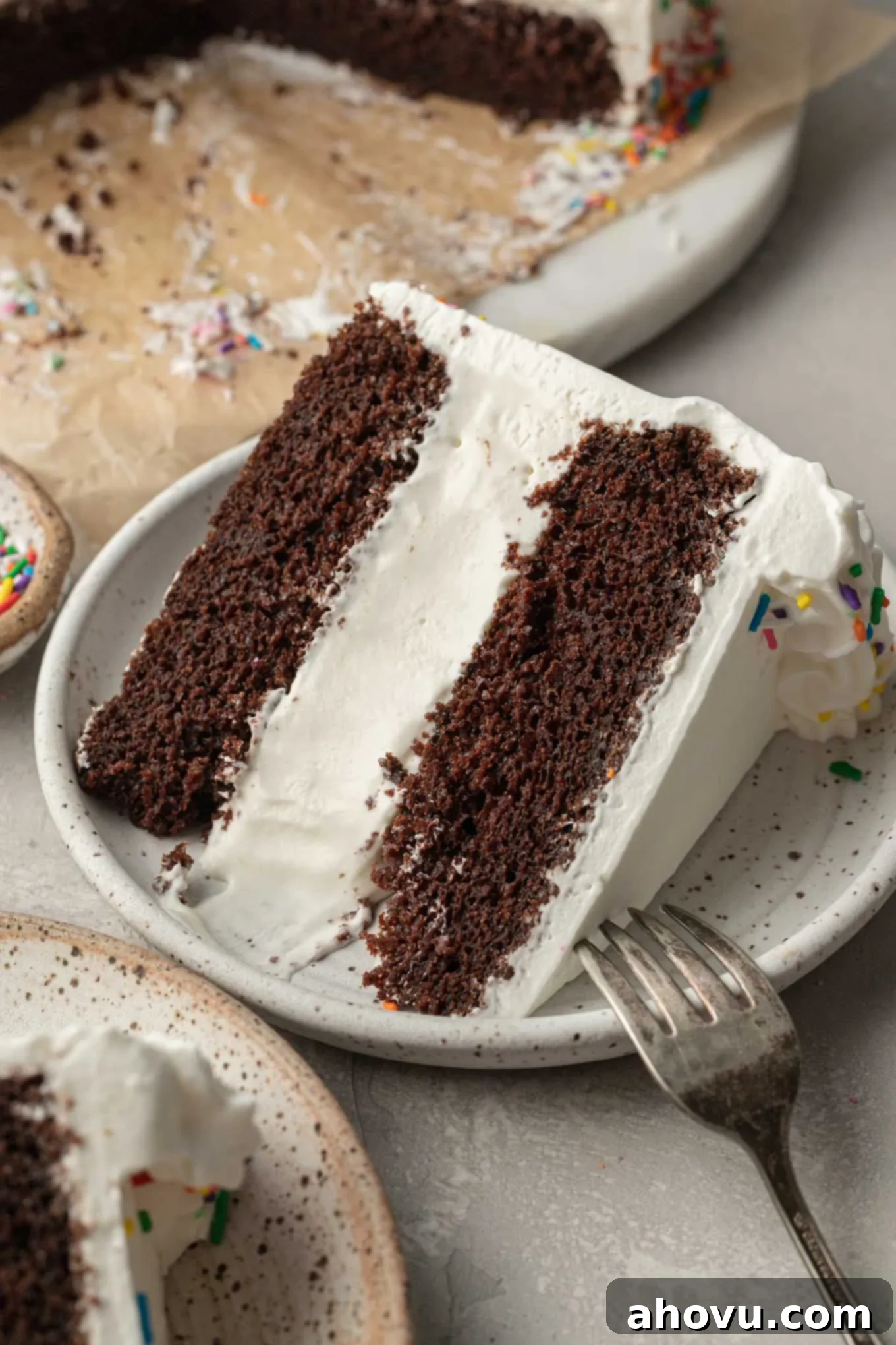 The Ultimate Homemade Ice Cream Cake 2 A slice of ice cream cake on a white plate with a fork next to it, showcasing the distinct layers of cake, ice cream, and frosting.