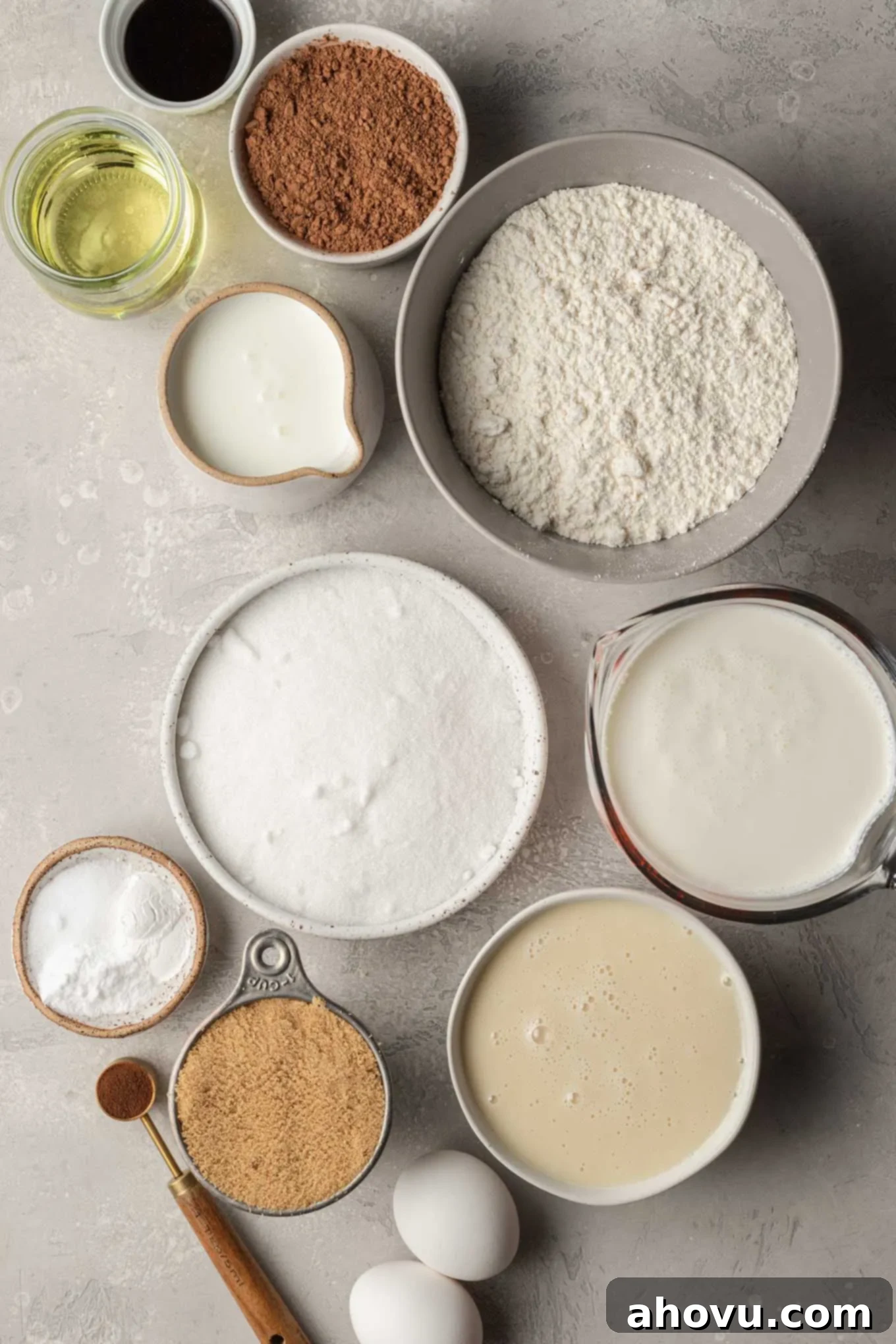 The Ultimate Homemade Ice Cream Cake 3 Various ingredients for an ice cream cake, including flour, cocoa, eggs, milk, and cream, neatly arranged on a gray surface.