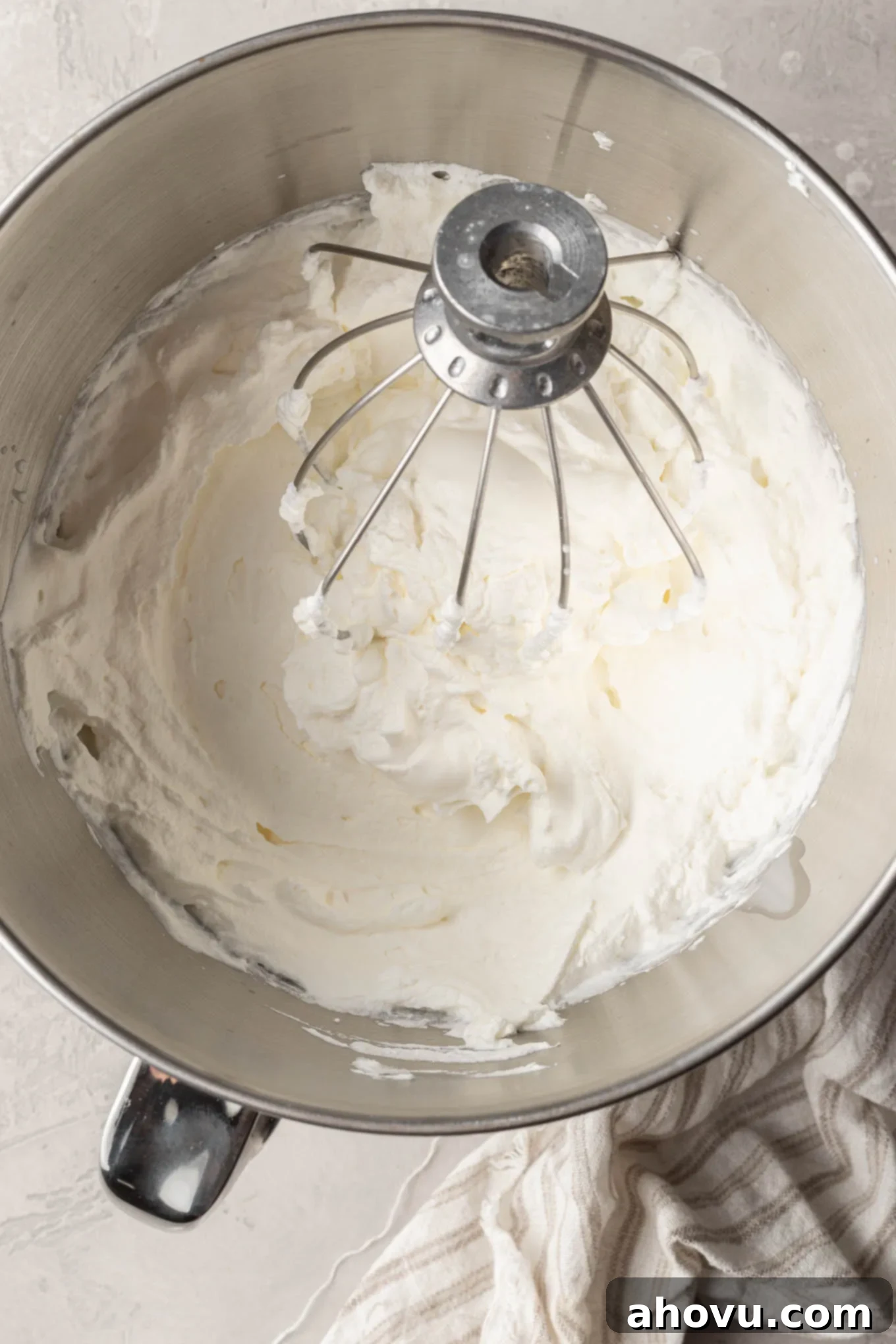 The Ultimate Homemade Ice Cream Cake 5 An overhead view of heavy whipping cream beaten to stiff peaks in the bowl of a stand mixer, demonstrating proper whipping consistency.
