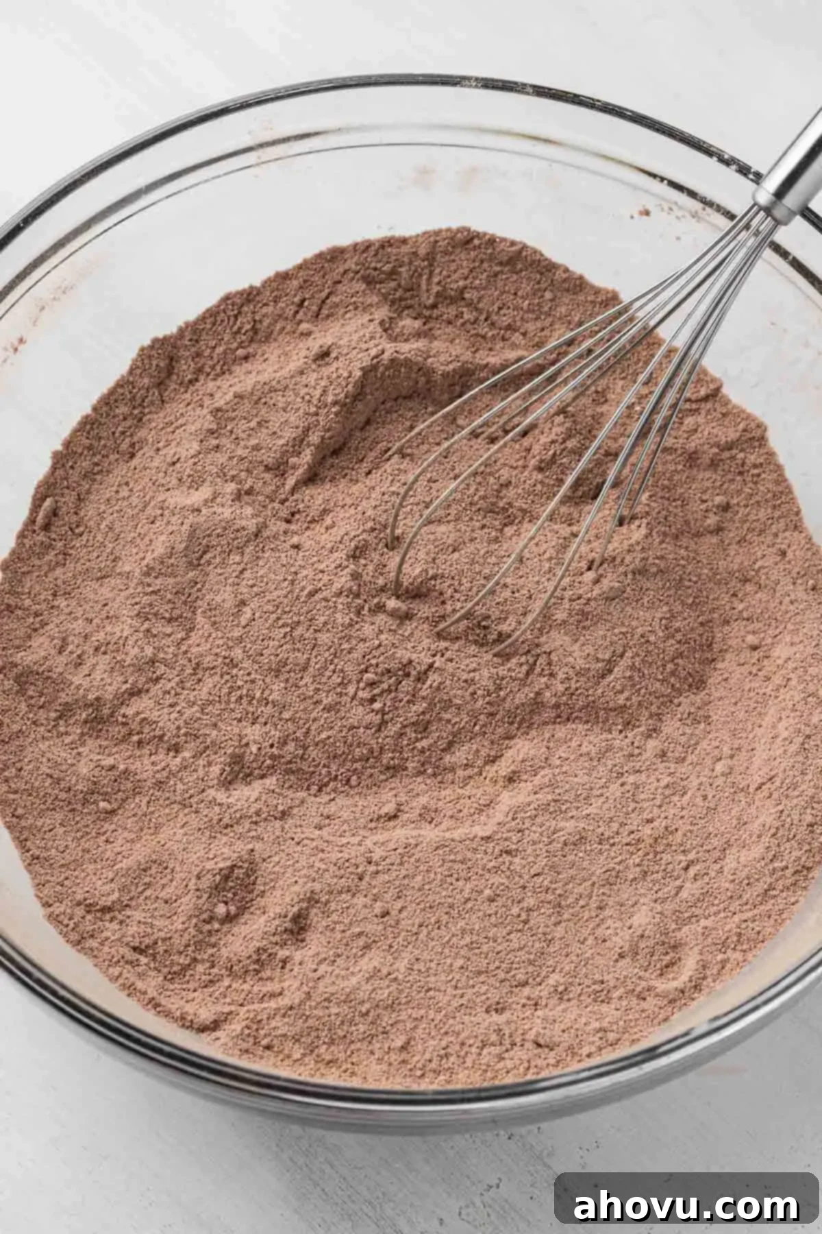 The Ultimate Homemade Ice Cream Cake 8 The dry ingredients for a rich chocolate cake, including flour, cocoa powder, and sugars, neatly arranged in a glass mixing bowl with a whisk.