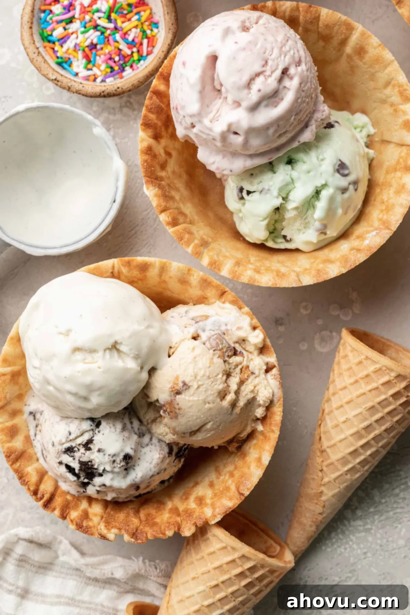 Two waffle cone bowls overflowing with scoops of homemade vanilla no-churn ice cream, garnished with fresh berries and chocolate shavings, viewed from above.