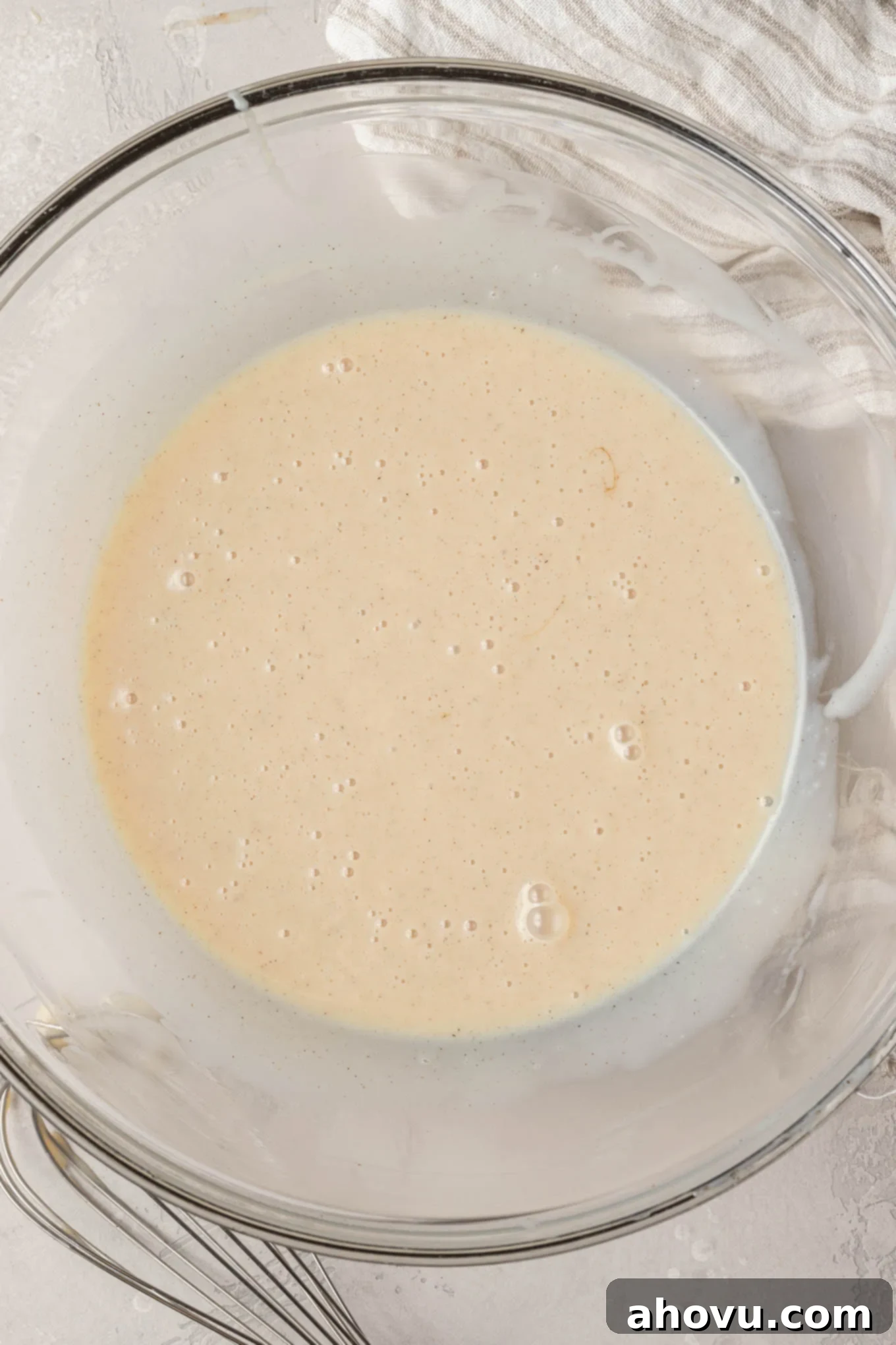 A glass mixing bowl holds a creamy mixture of sweetened condensed milk, golden vanilla extract, and a sprinkle of salt, perfectly whisked together.