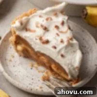 A slice of banoffee pie on a speckled white plate with a fork resting on the side.