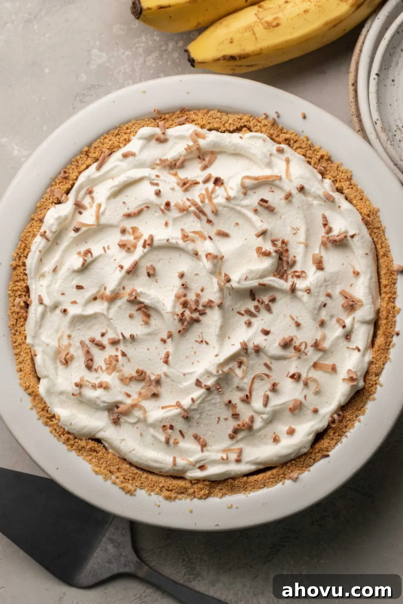 An overhead view of a completed banoffee pie, beautifully topped with delicate chocolate shavings, ready for chilling. 