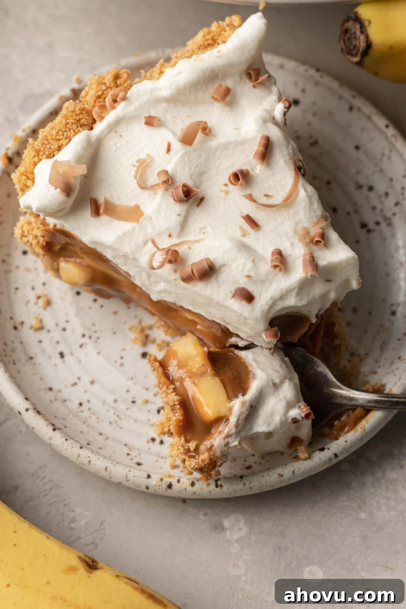 A close-up of a slice of banoffee pie on a speckled dessert plate, with a fork gently taking a bite, emphasizing its delicious layers. 