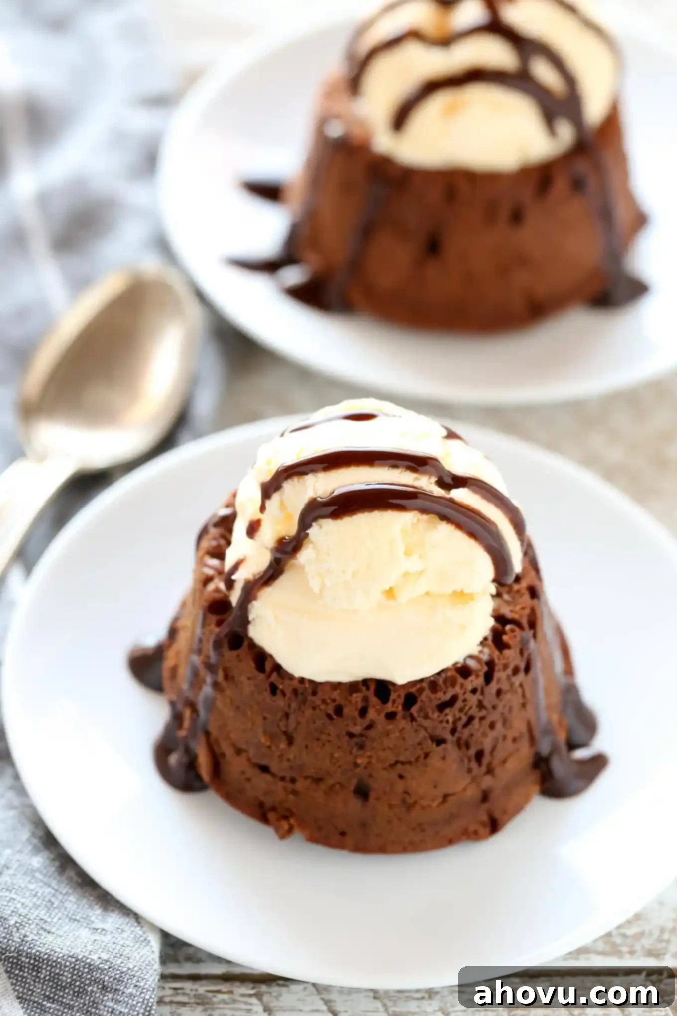 Two perfectly baked chocolate lava cakes topped with a scoop of vanilla ice cream and a luscious drizzle of chocolate sauce. Both individual desserts are presented on elegant white dessert plates, highlighting their exquisite appeal.
