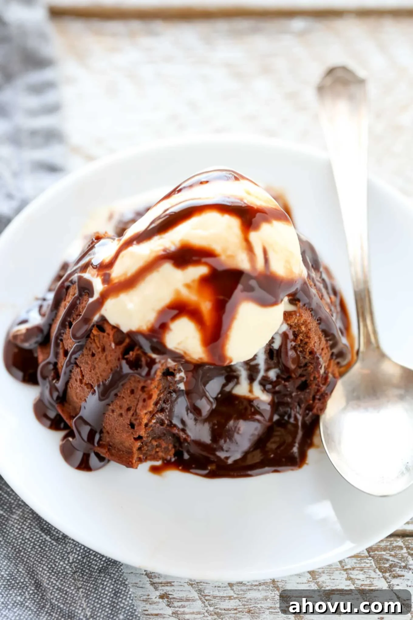 Another close-up shot of a molten lava cake served on a white plate, adorned with a scoop of vanilla ice cream and a rich chocolate sauce. The cake has been sliced, revealing the delightful cascade of molten chocolate from its core.