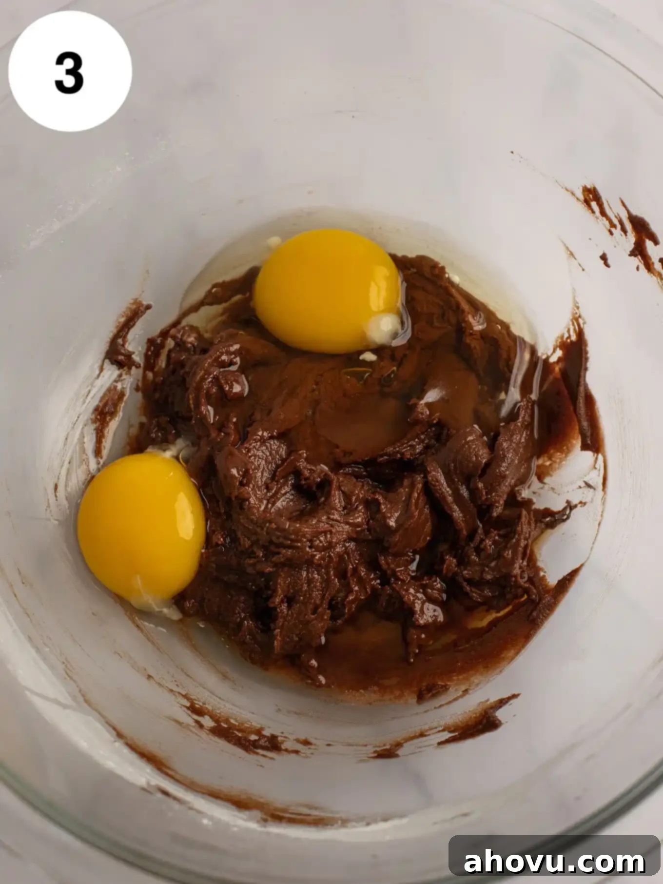 The smooth chocolate batter in a glass bowl, with a whole egg and an egg yolk resting on top, ready to be mixed in.