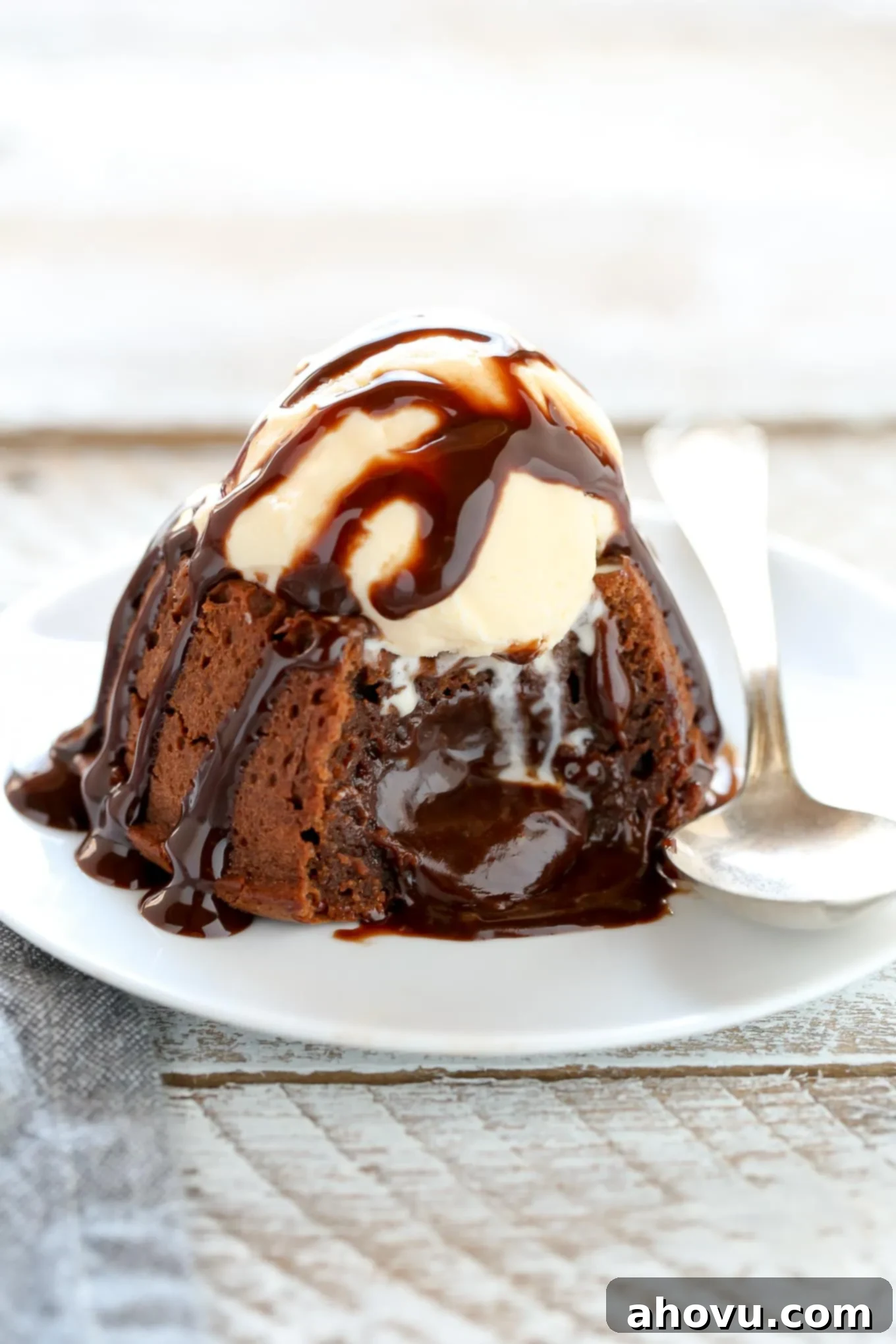A perfectly baked molten chocolate lava cake, freshly inverted onto a white plate, revealing its rich, dark exterior. The cake has been cut into, and the warm, liquid chocolate filling is oozing out enticingly.