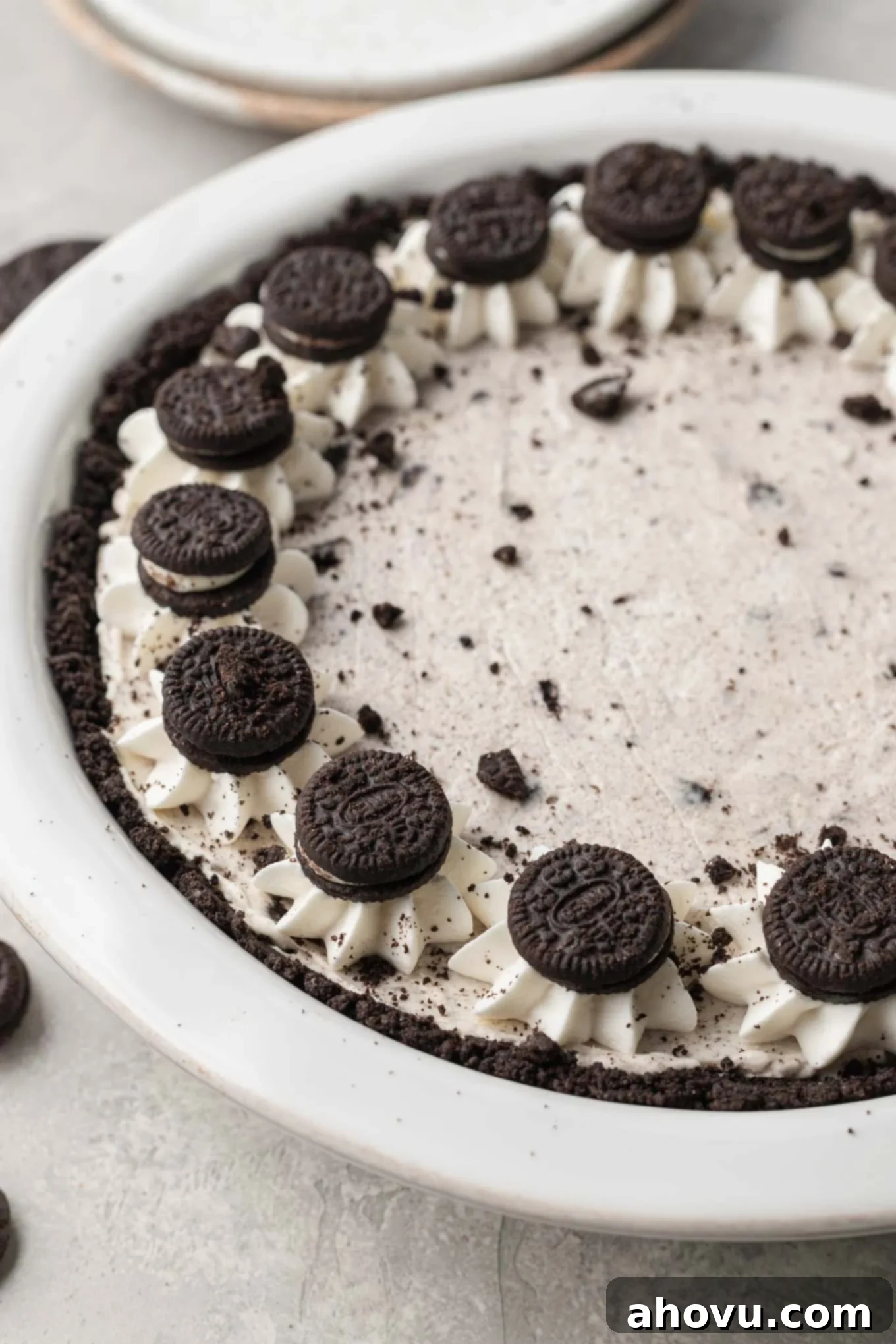 A side view of a decadent Oreo pie, beautifully garnished with swirls of whipped cream piped around the edges and mini Oreos pressed artfully on top of the whipped cream, showcasing its rich texture and tempting layers.