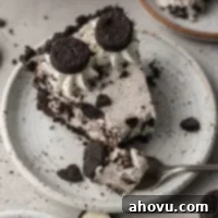 A slice of Oreo pie on a white speckled plate. A fork with a piece of the pie rests on the plate.