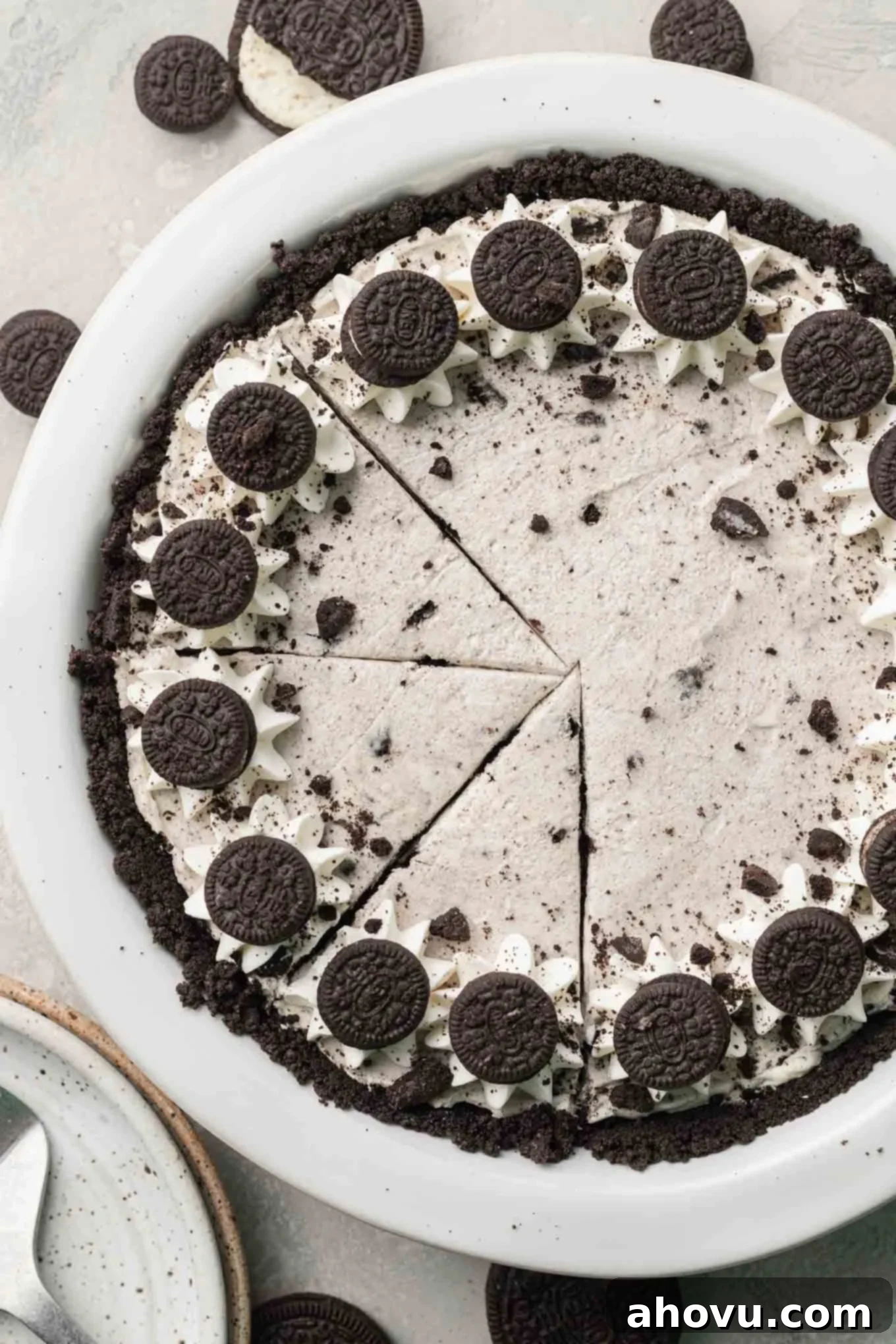 An overhead view of a beautifully sliced Oreo pie, revealing its distinct layers of dark Oreo crust and creamy white-and-black speckled filling, adorned with whipped cream and more Oreos.
