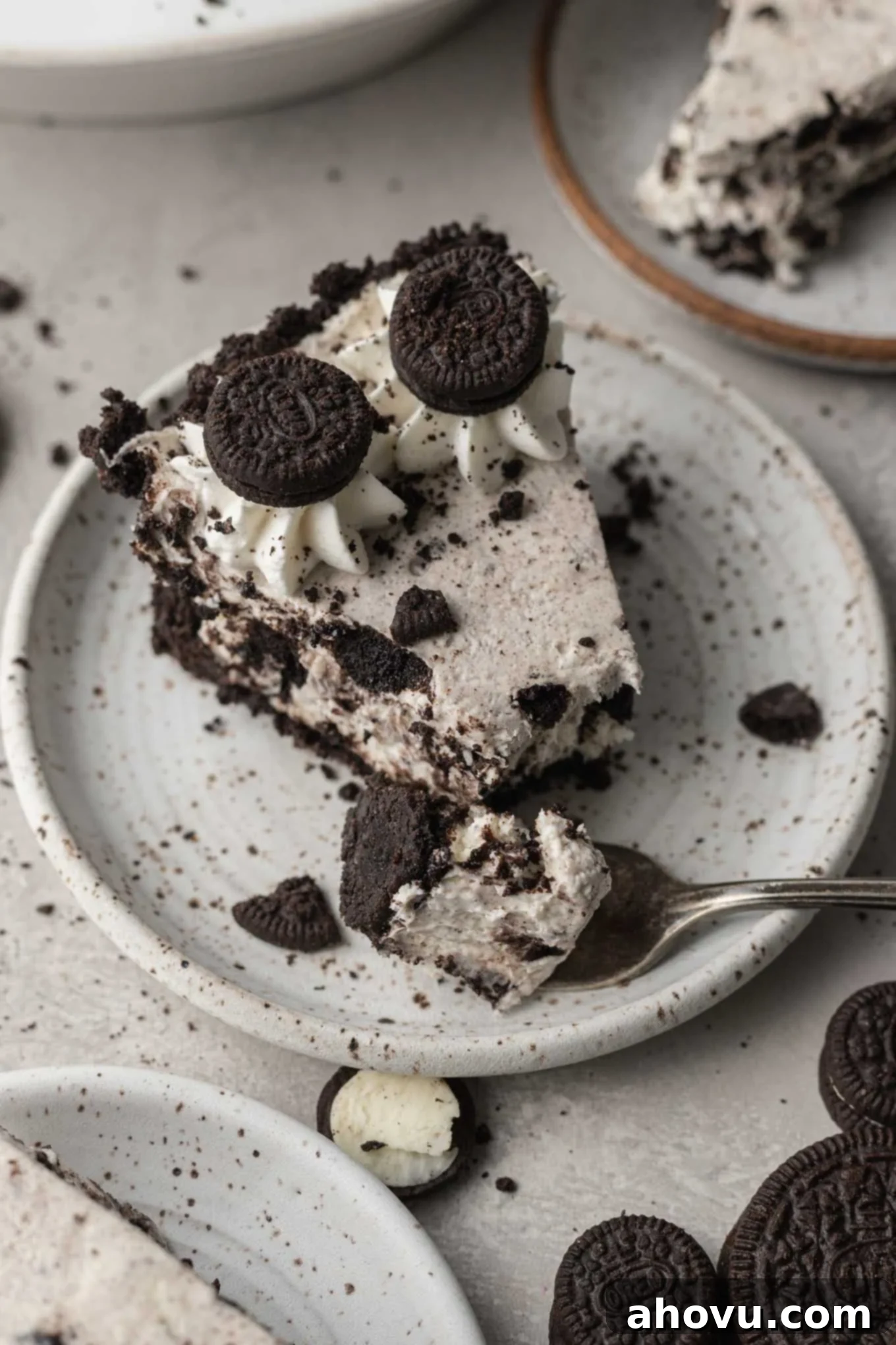 A perfect slice of Oreo pie resting on a speckled white dessert plate. A piece of the pie has been delicately removed with a fork, which now rests on the plate, highlighting the creamy texture and delicious layers.
