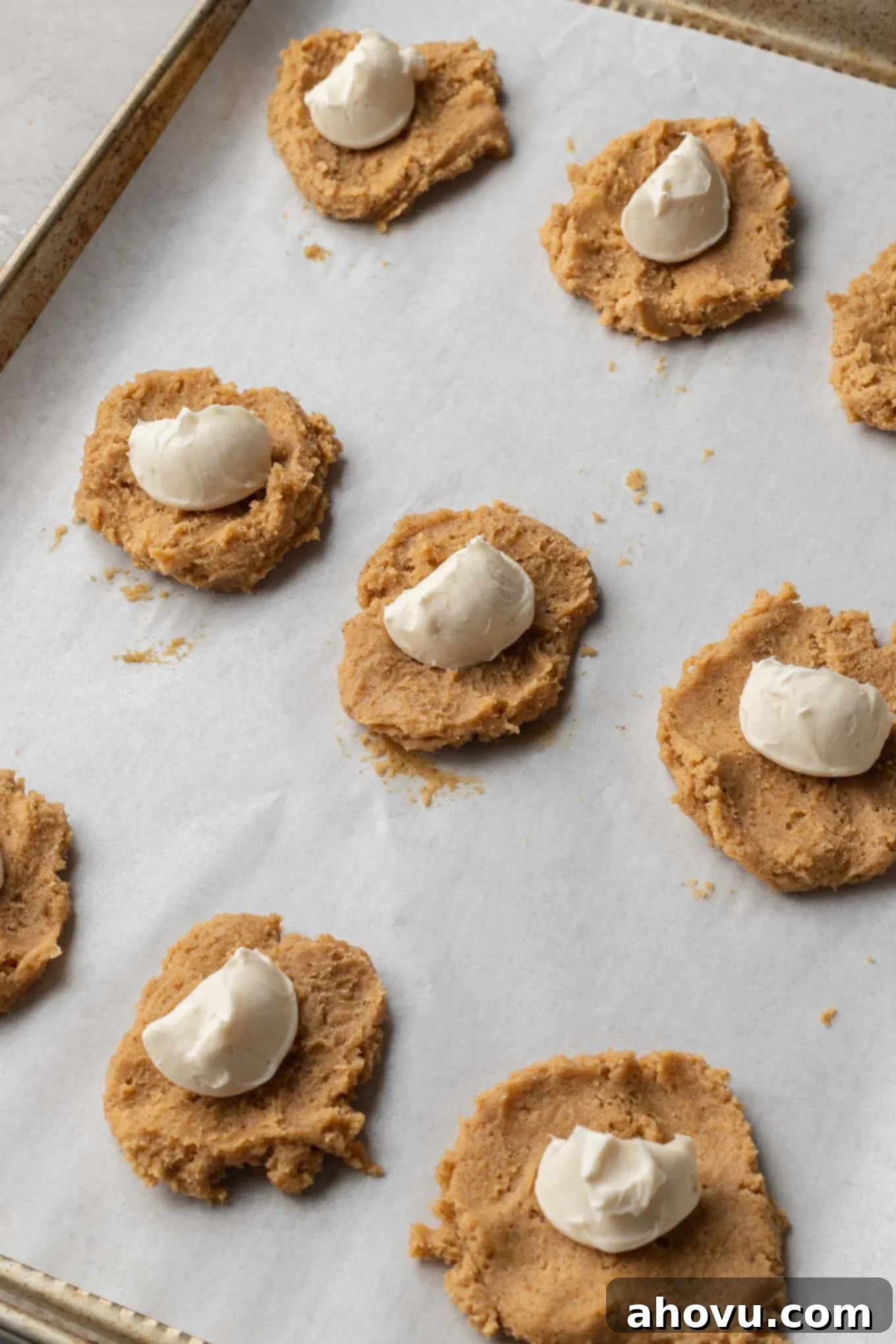 An overhead view of flattened balls of cookie dough with scoops of cream cheese in the center. 