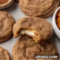 Pumpkin cheesecake cookies on a gray surface. One cookie has a bite missing to show the cream cheese center.