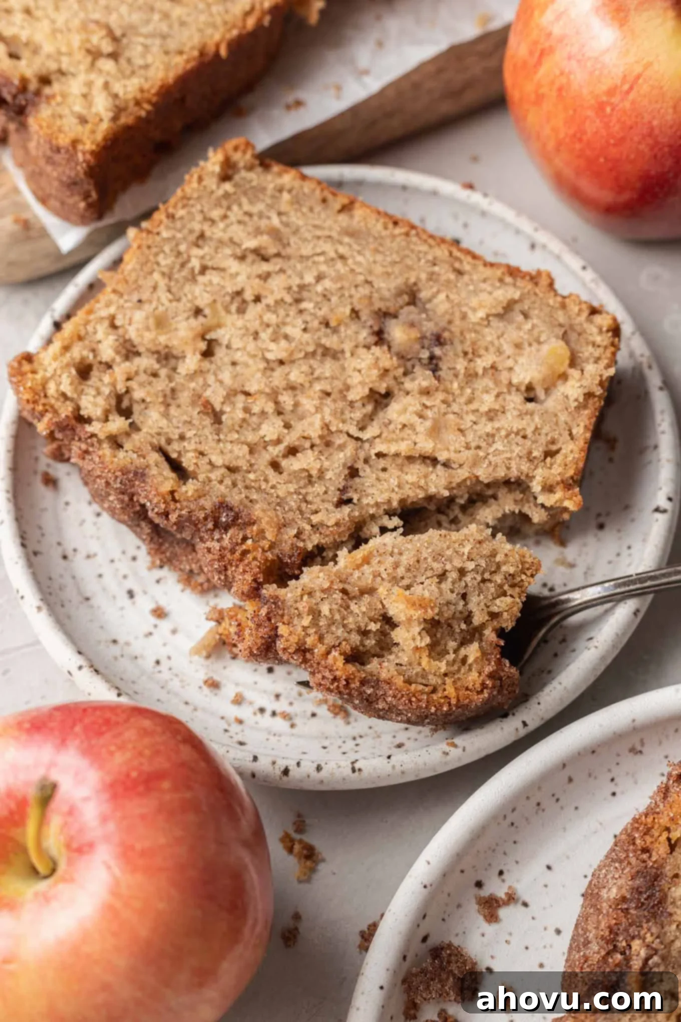 A slice of apple bread on a speckled dessert plate, with a fork. 