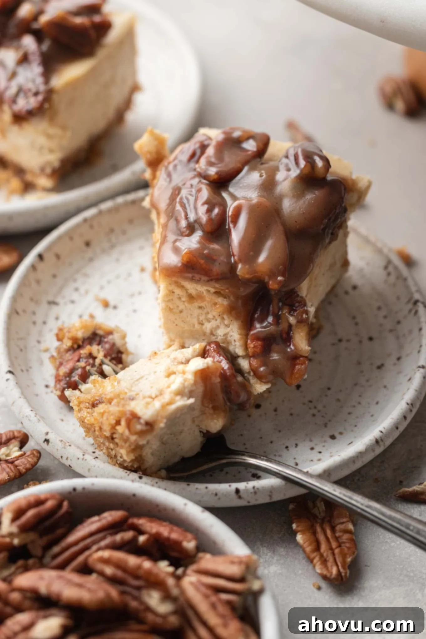 A slice of cheesecake with pecan topping on a speckled dessert plate. 