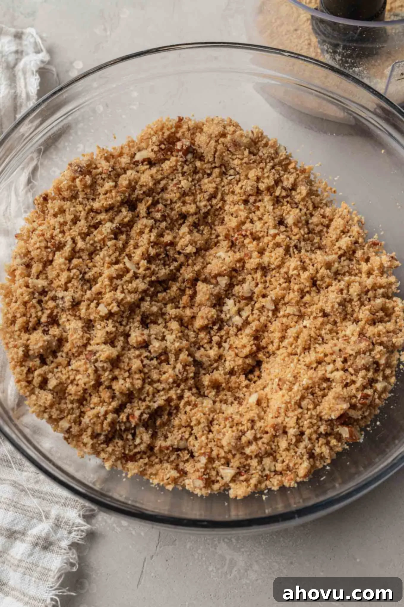 An overhead view of a graham cracker crust mixture in a glass mixing bowl. 