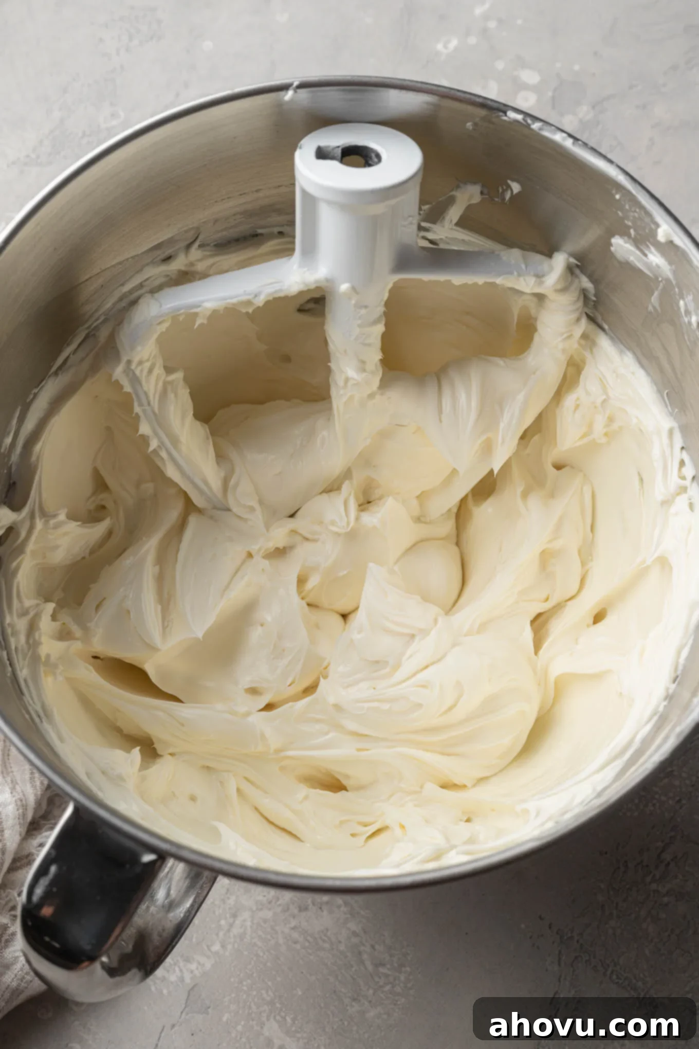 An overhead view of beaten cream cheese and sour cream in the bowl of a stand mixer, with a paddle attachment. 